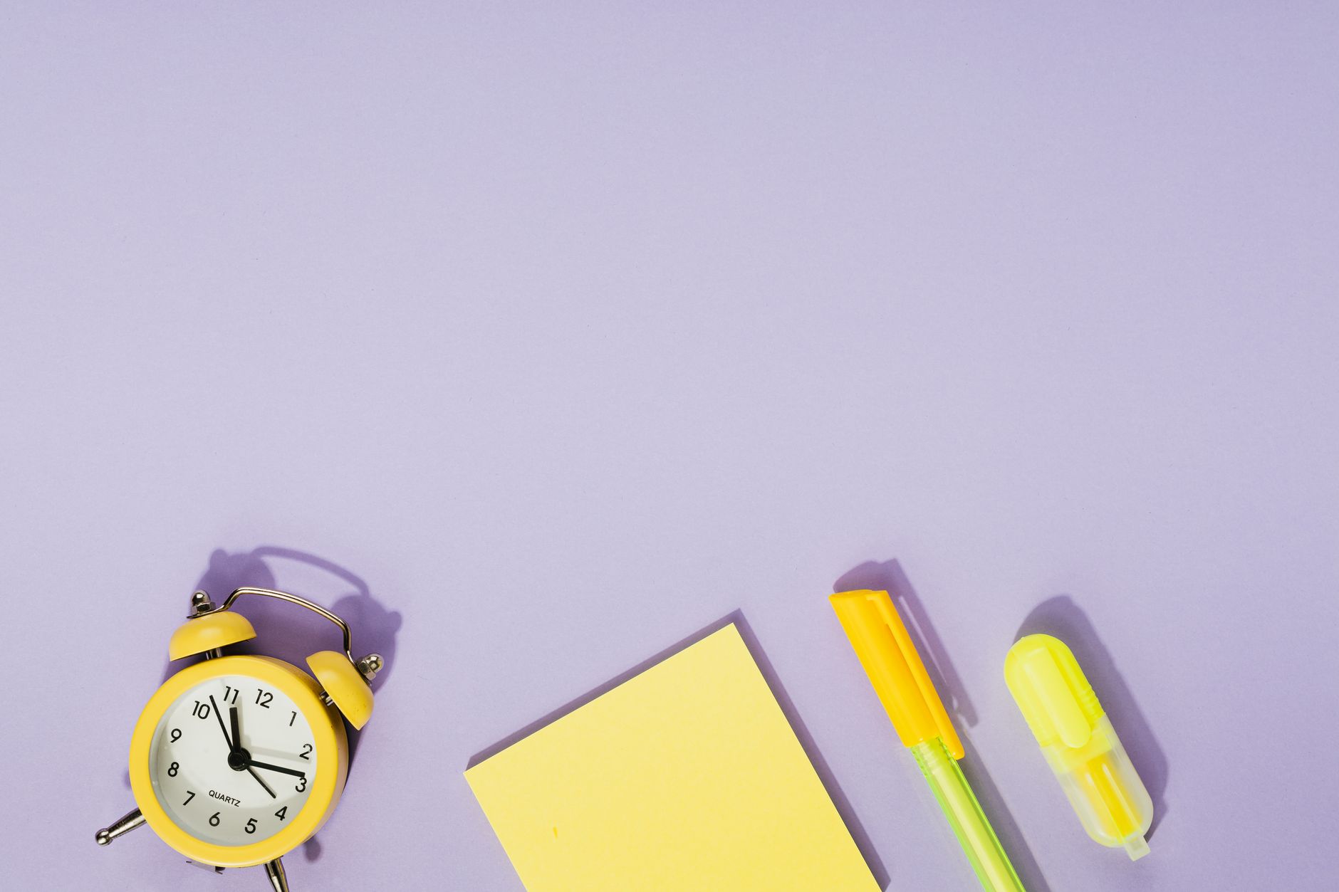 Vibrant desk setup with a yellow alarm clock, sticky notes, and stationery on a purple background.