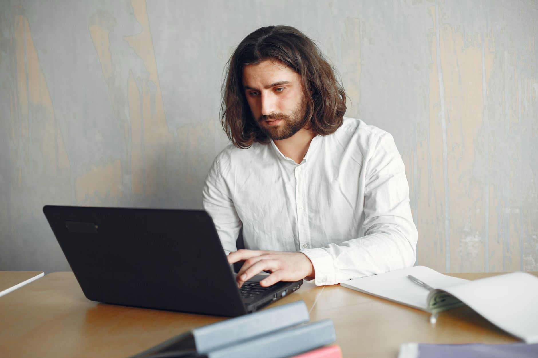 A bearded man working remotely on his laptop at a desk with documents, showcasing a modern work setting.