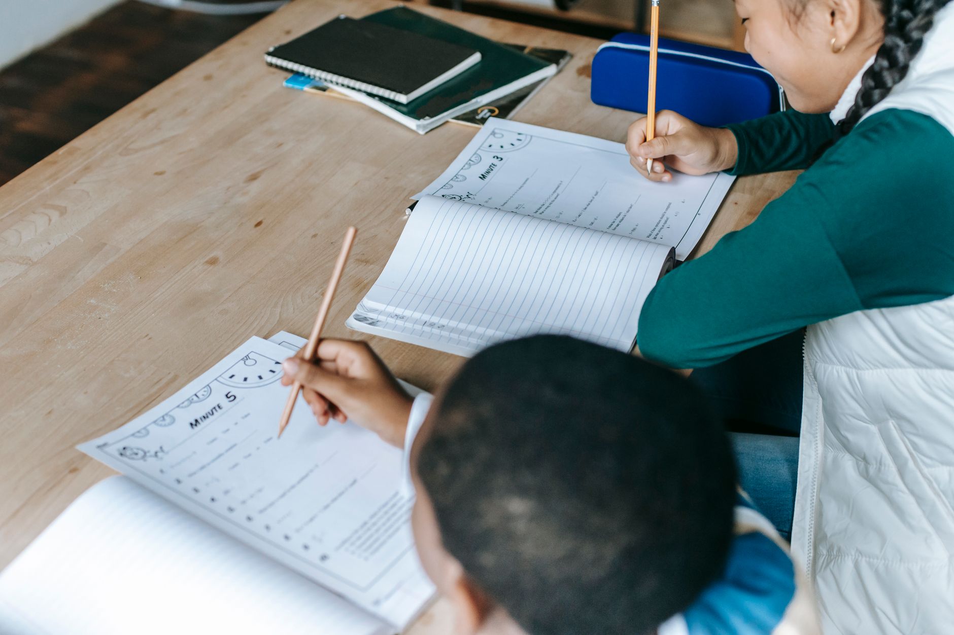 From above of diverse smart boy and girl doing tasks and writing on papers at classroom desk