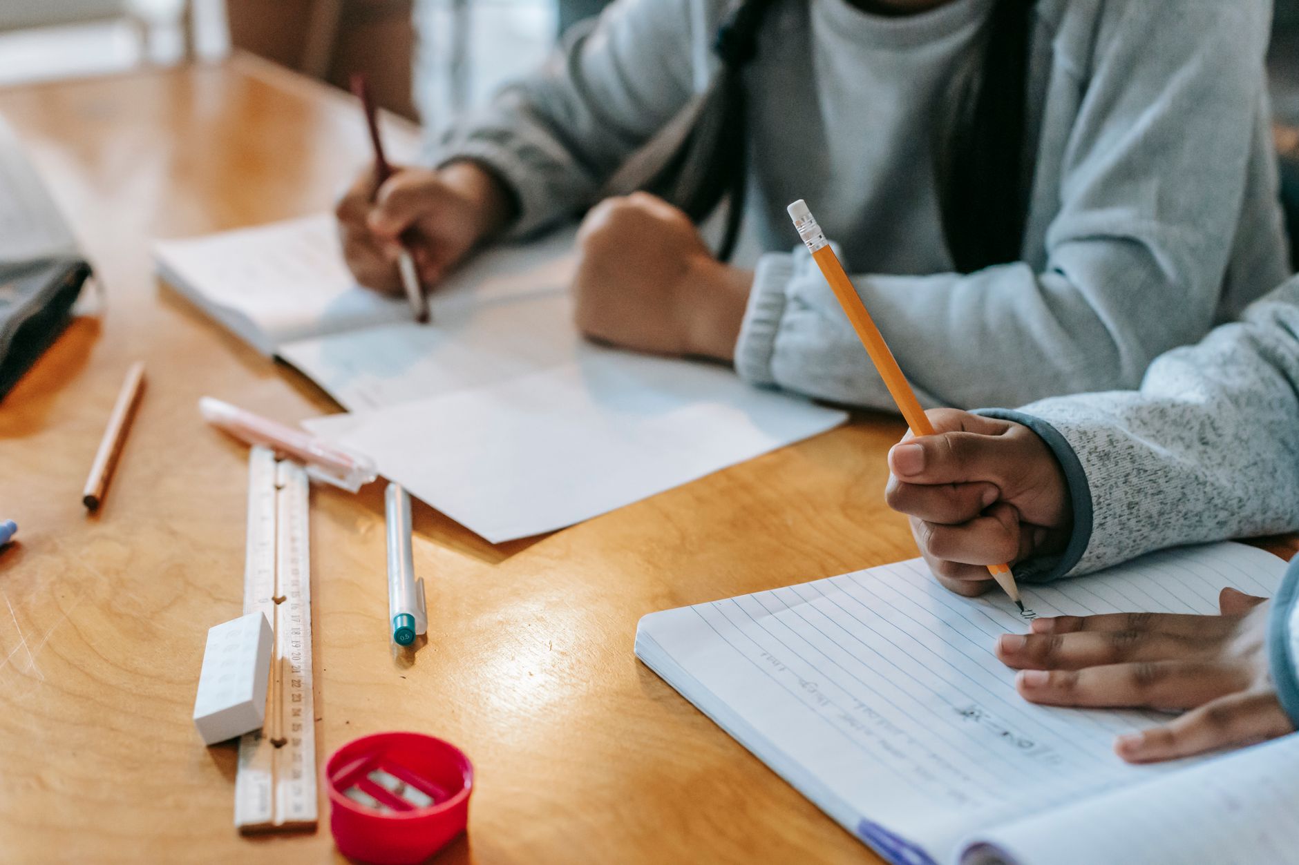 Crop unrecognizable schoolchildren sitting at wooden table and writing notes during lesson at school