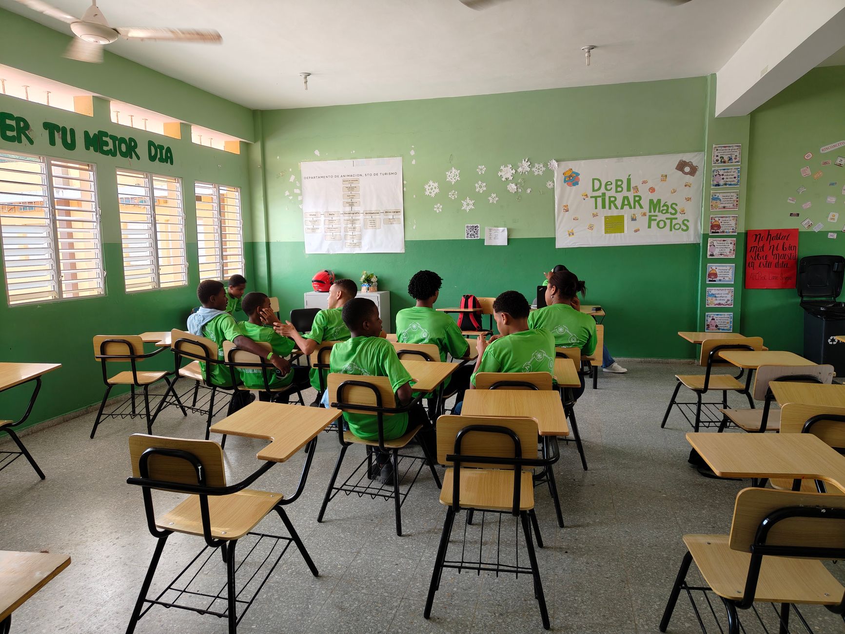 Children in a classroom attending a lesson, wearing green uniforms. Educational setup.