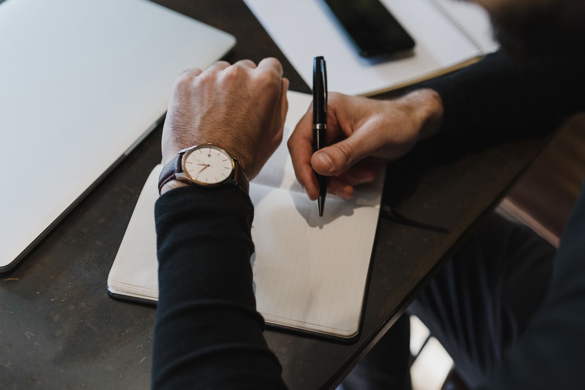 Close-up of a person writing in a notebook, wearing a watch, top view.