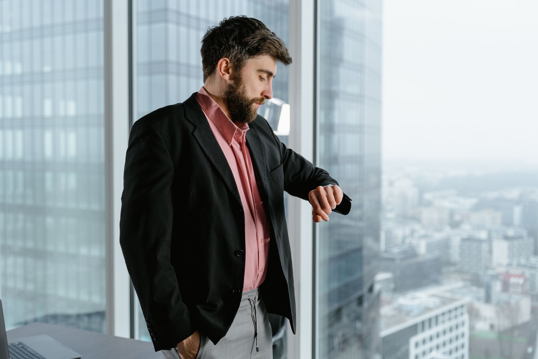 Confident businessman in an office looking at his watch by a large window with a city view.