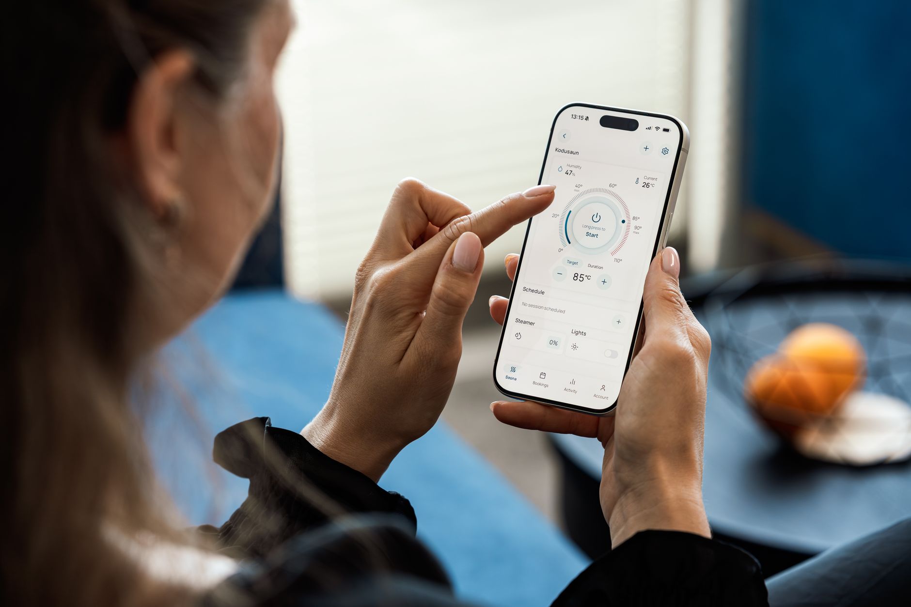 A woman uses a smartphone app to adjust her sauna settings indoors.