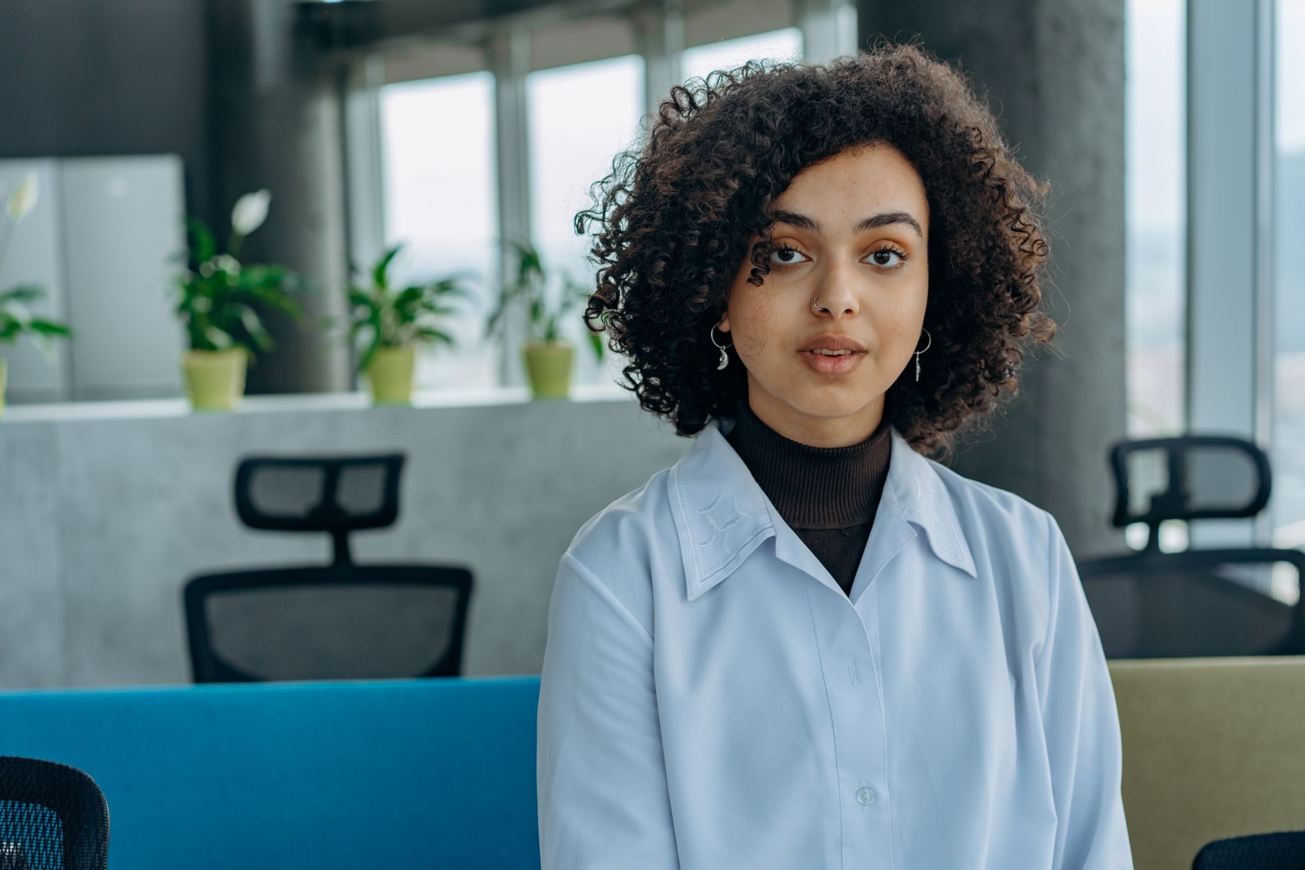 Portrait of a young woman with curly hair in a modern office space, conveying professionalism.