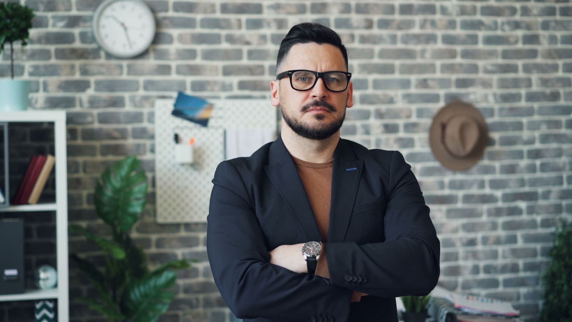 Businessman with beard and glasses stands confidently in office setting.