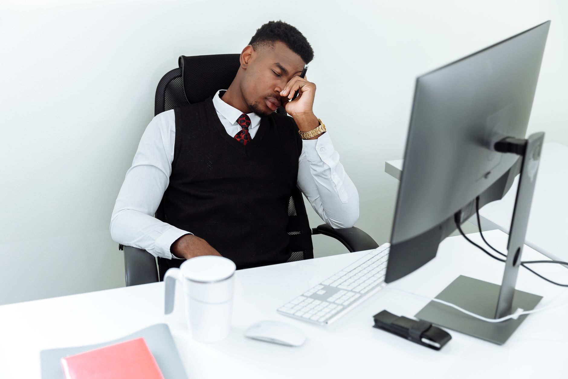 A man in business attire resting his head at an office desk, displaying workplace fatigue.