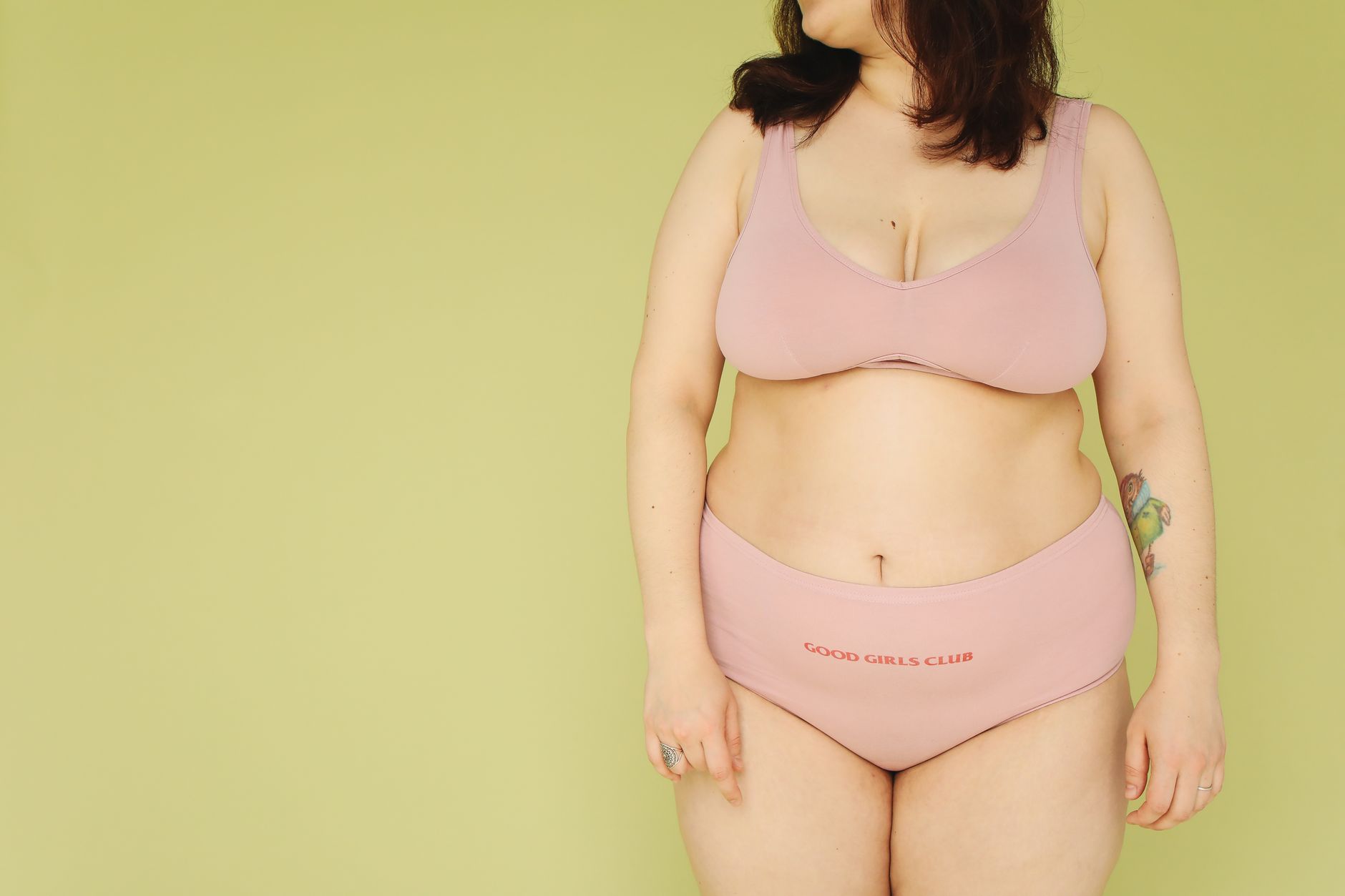 Confident plus size woman modeling pink lingerie against yellow backdrop.