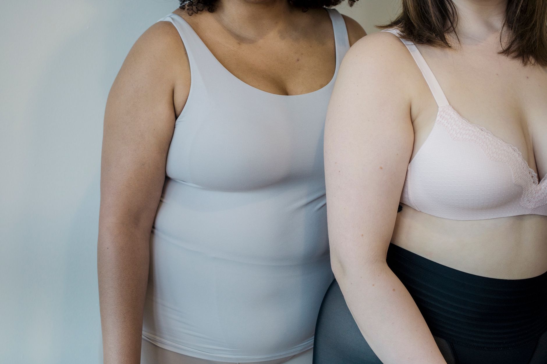Crop anonymous multiracial plus size girlfriends in bra and undershirt standing close on light background