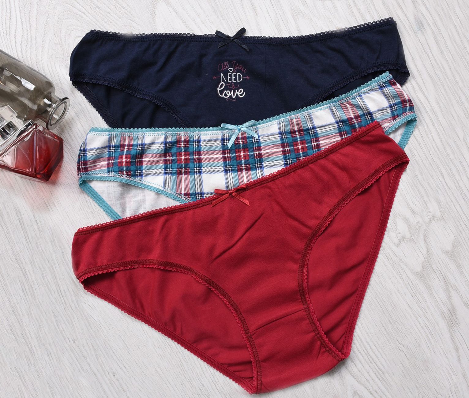 Three pairs of colorful women's underwear on a light wooden floor with a glass bottle.
