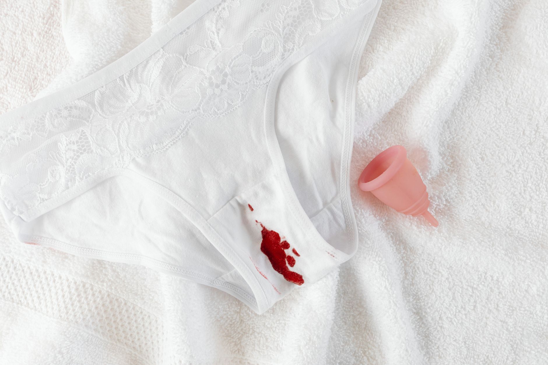 A menstrual cup alongside stained underwear on a clean towel, symbolizing menstrual health.