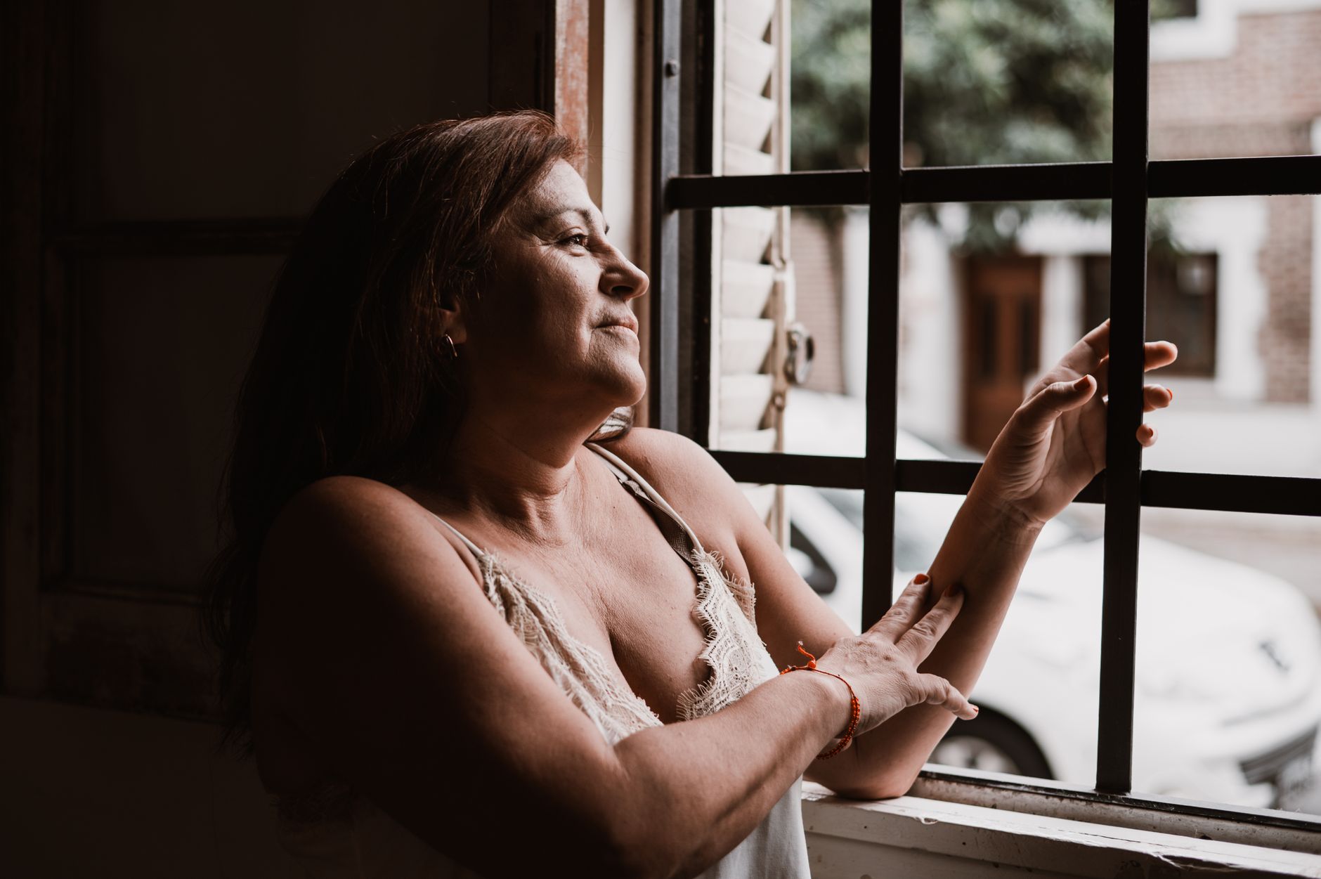 A thoughtful woman looking out of a window in Provincia de Buenos Aires, evoking reflection and serenity.