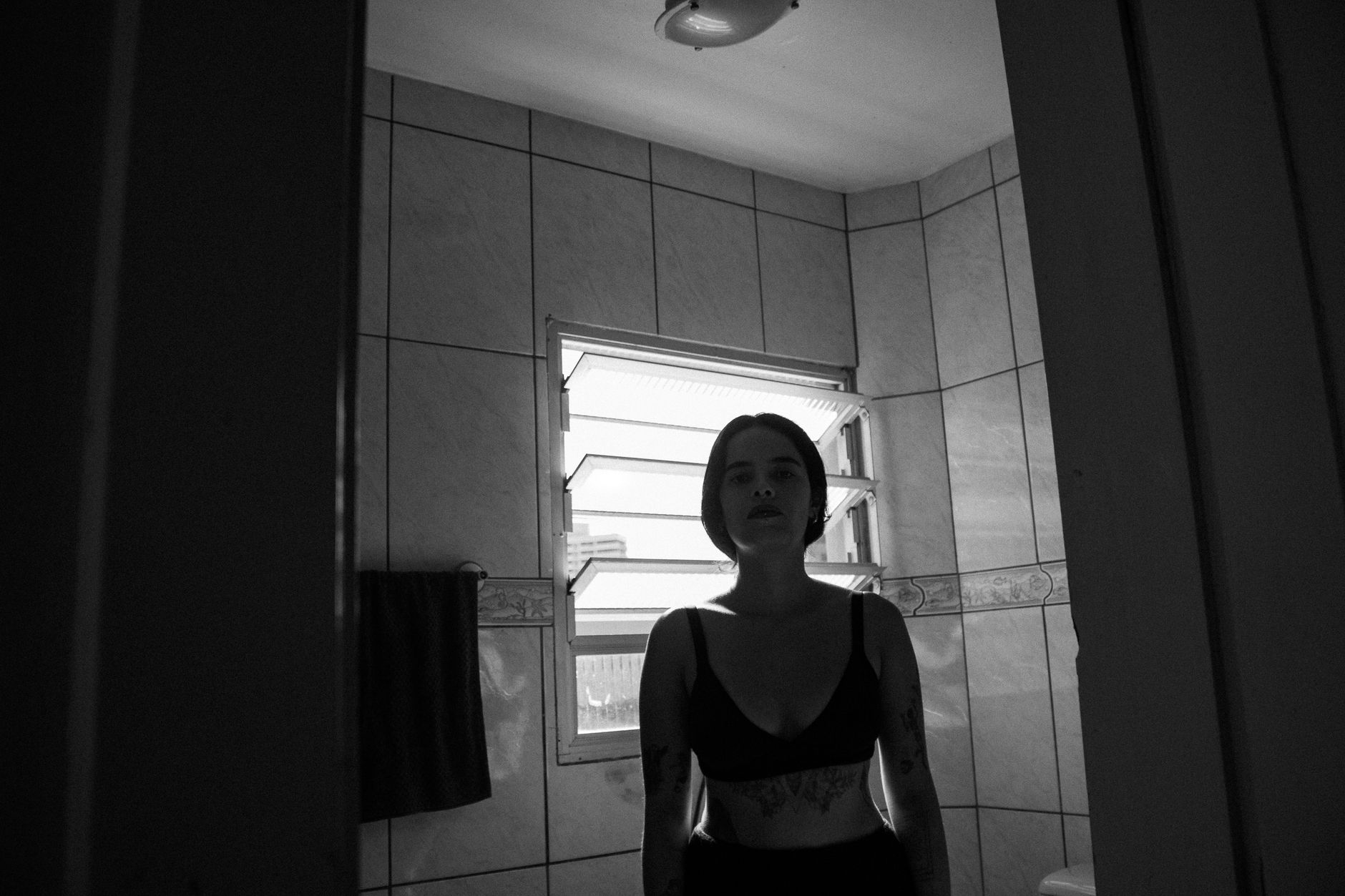 A woman stands alone in a dark bathroom, creating a moody ambiance.