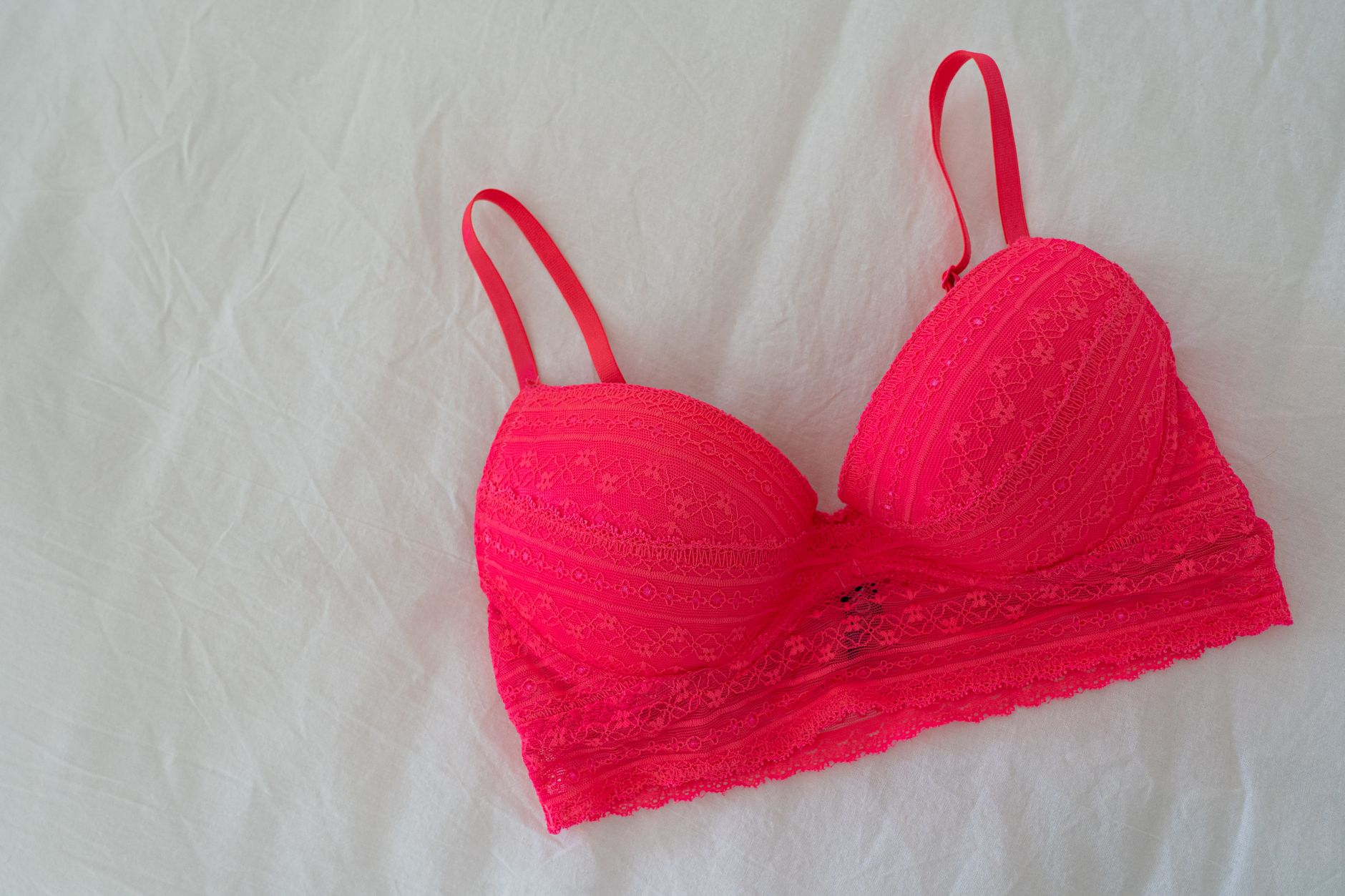Bright lace pink bra laid flat on soft white sheet.
