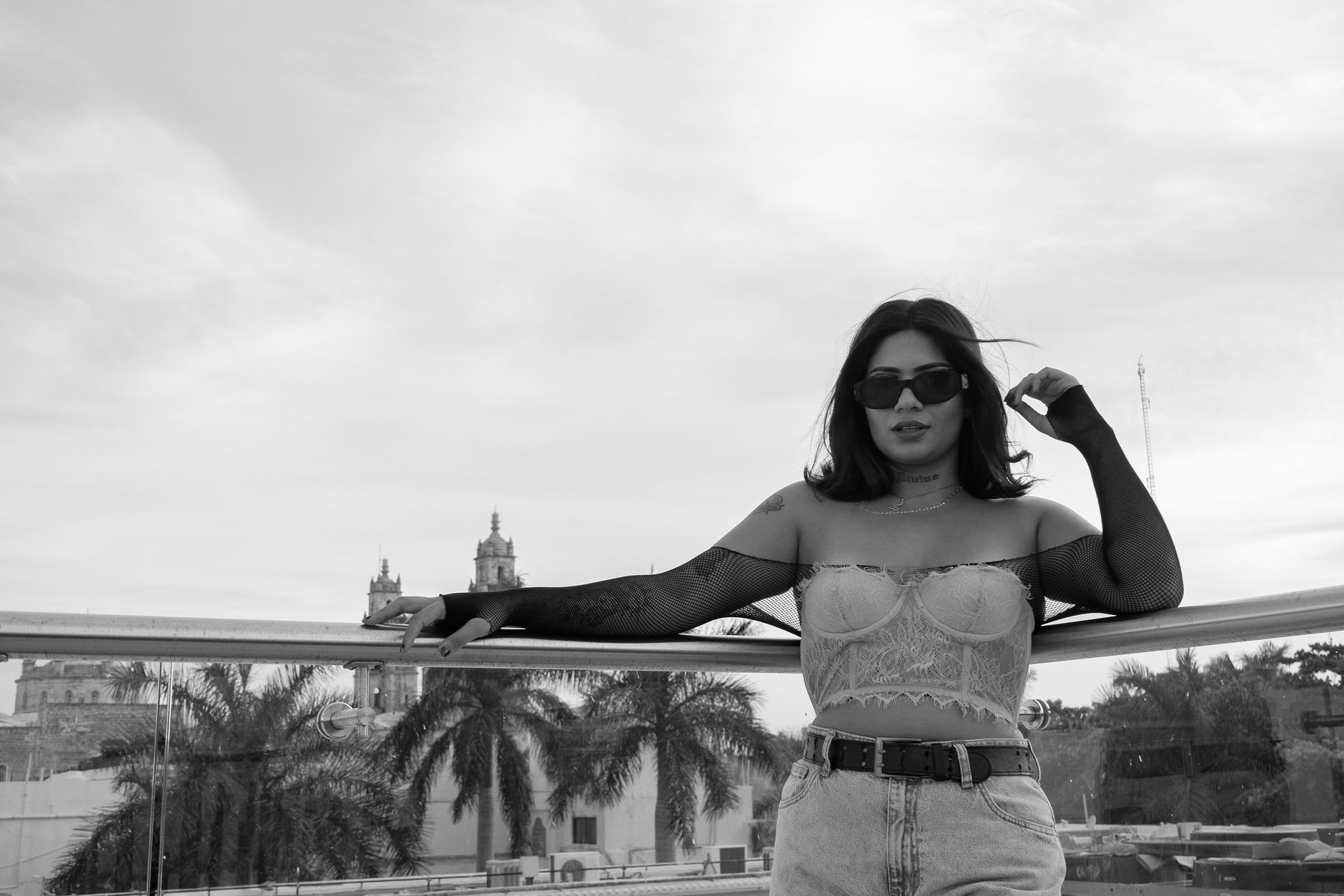 Stylish woman in corset poses on a rooftop terrace in Mérida, Mexico. Palm trees and cityscape in background.