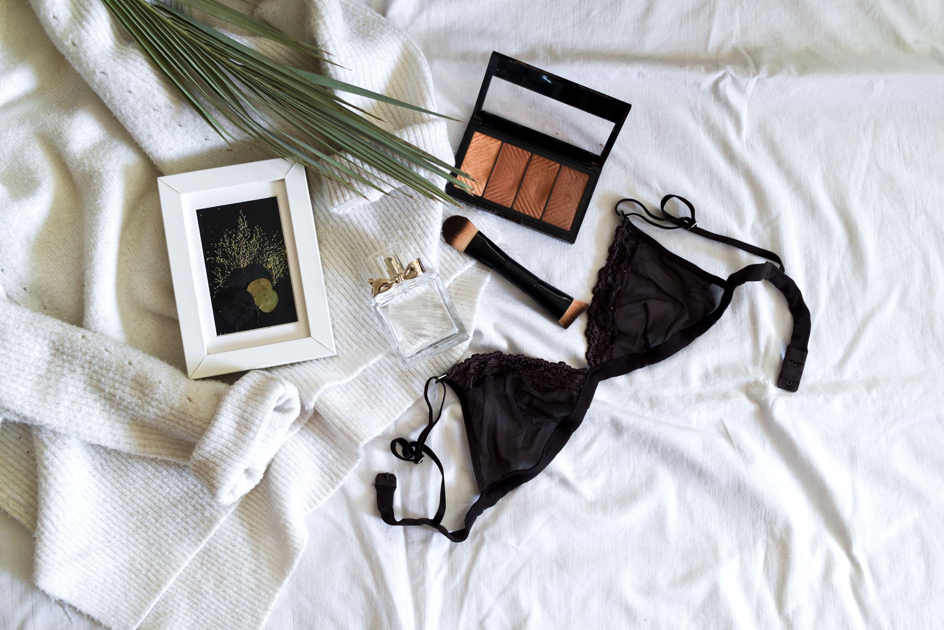 A stylish flat lay of lingerie, makeup, and accessories on a soft background.