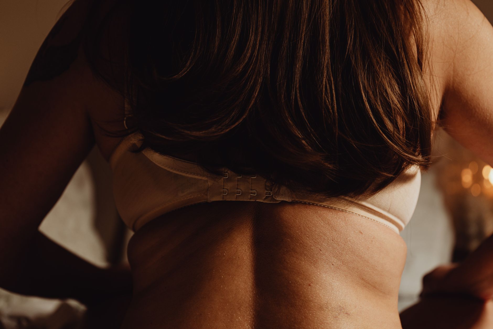 Detailed close-up image of a woman's back wearing a bra in warm lighting.