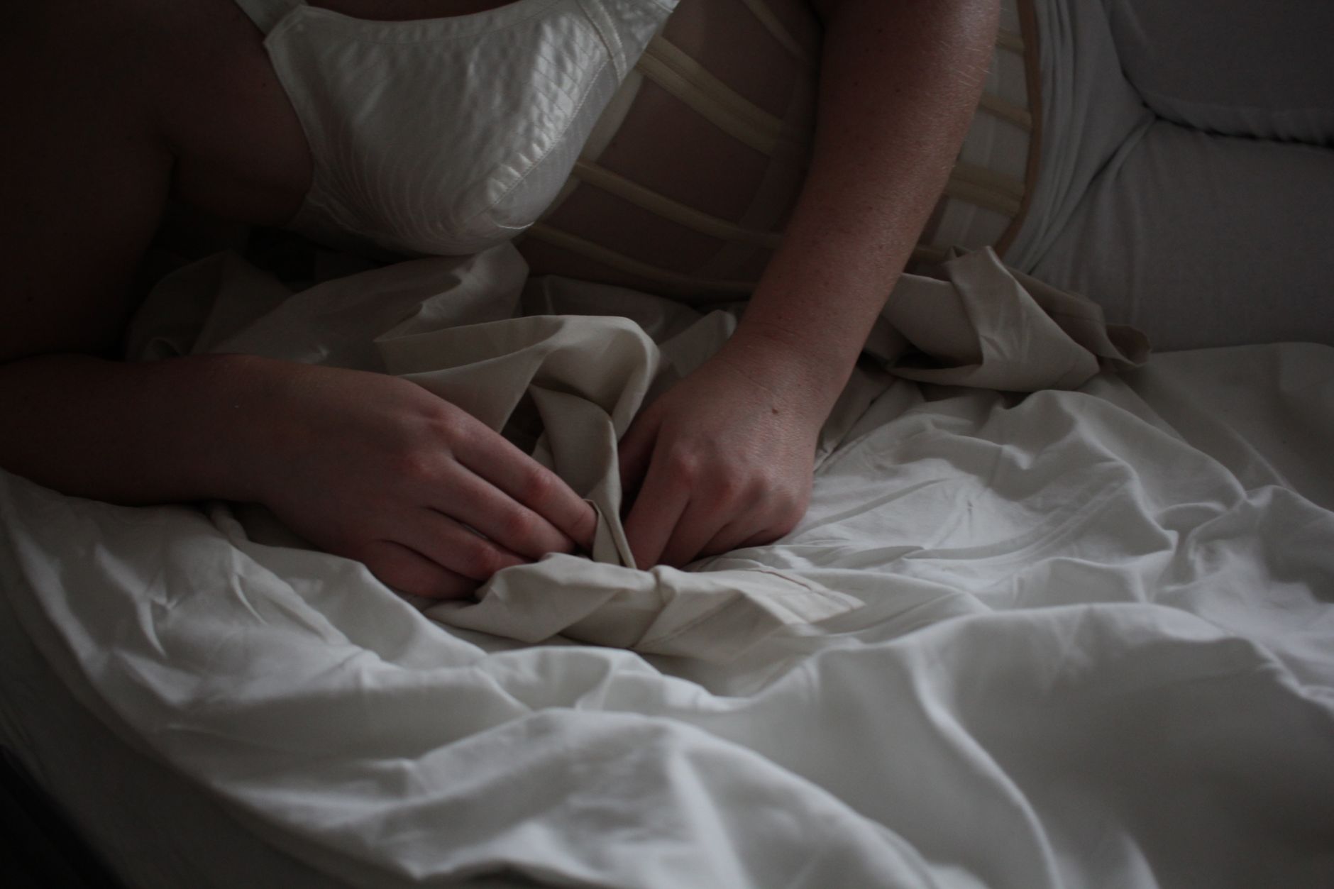 A person in lingerie lying on white bed linens, capturing a serene and intimate moment.