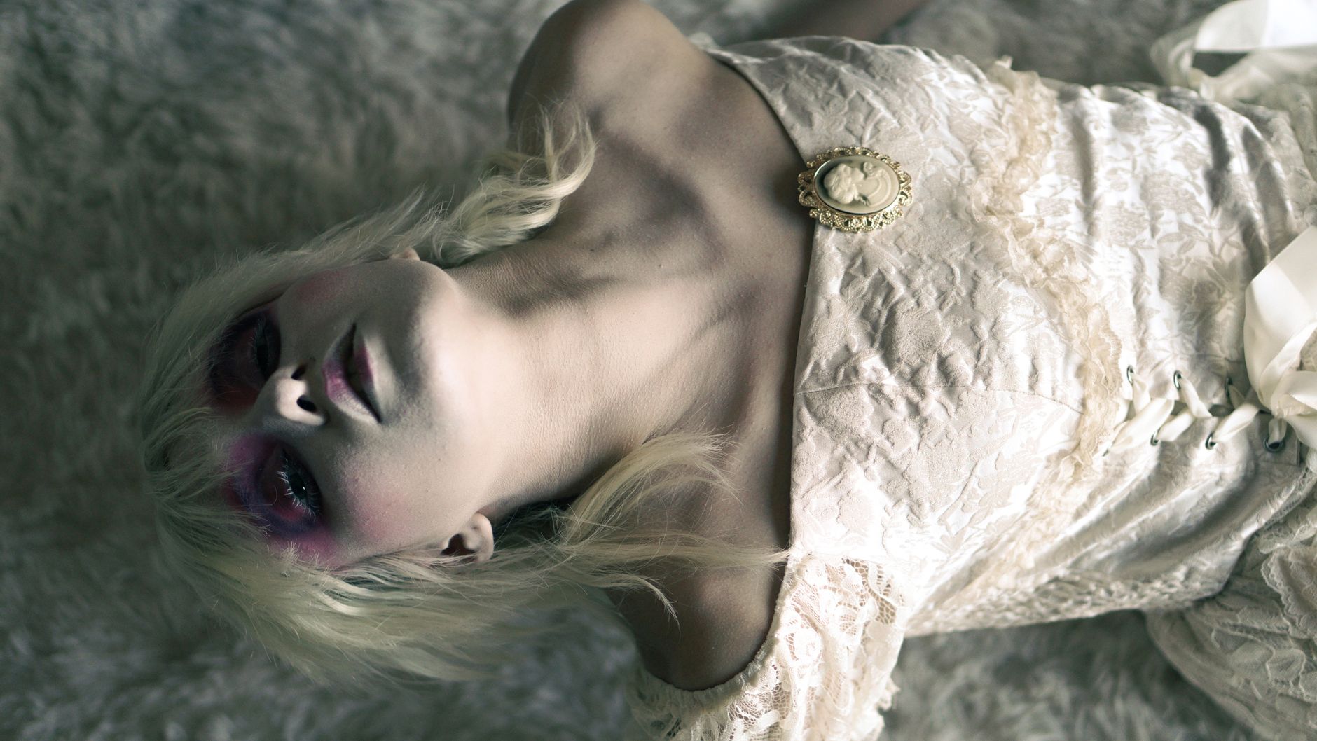 An artistic portrait depicting a woman in a vintage lace dress with dramatic makeup and a cameo brooch.