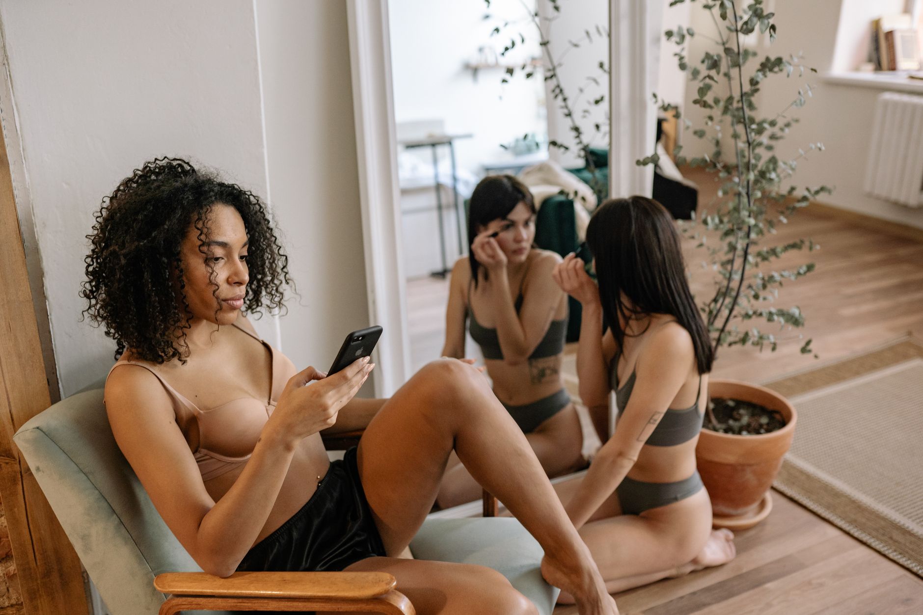 Three young women in comfortable lingerie enjoying a casual moment indoors with a mirror.