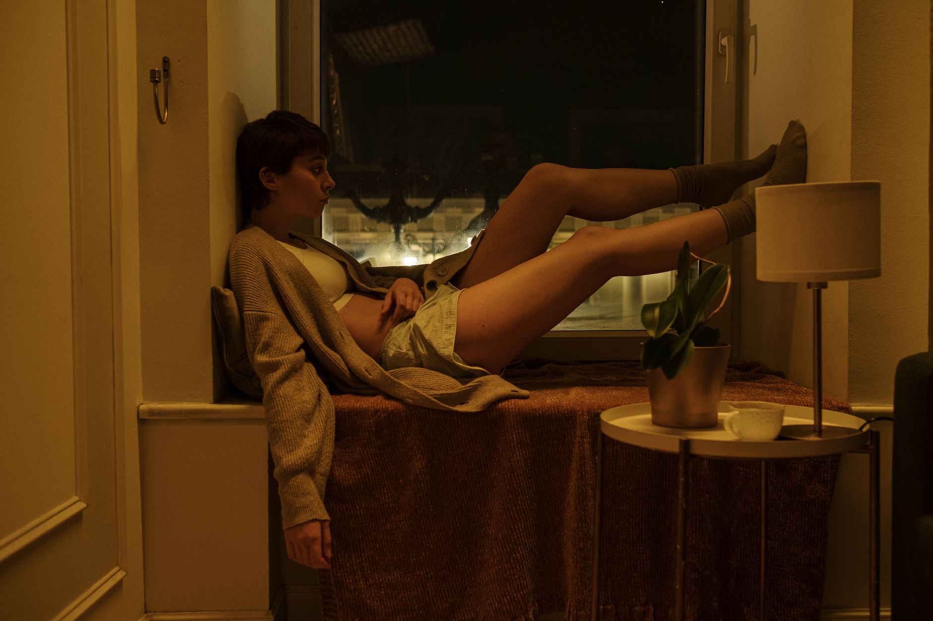 A woman sits by a window at night, exuding a vibe of tranquility and introspection.