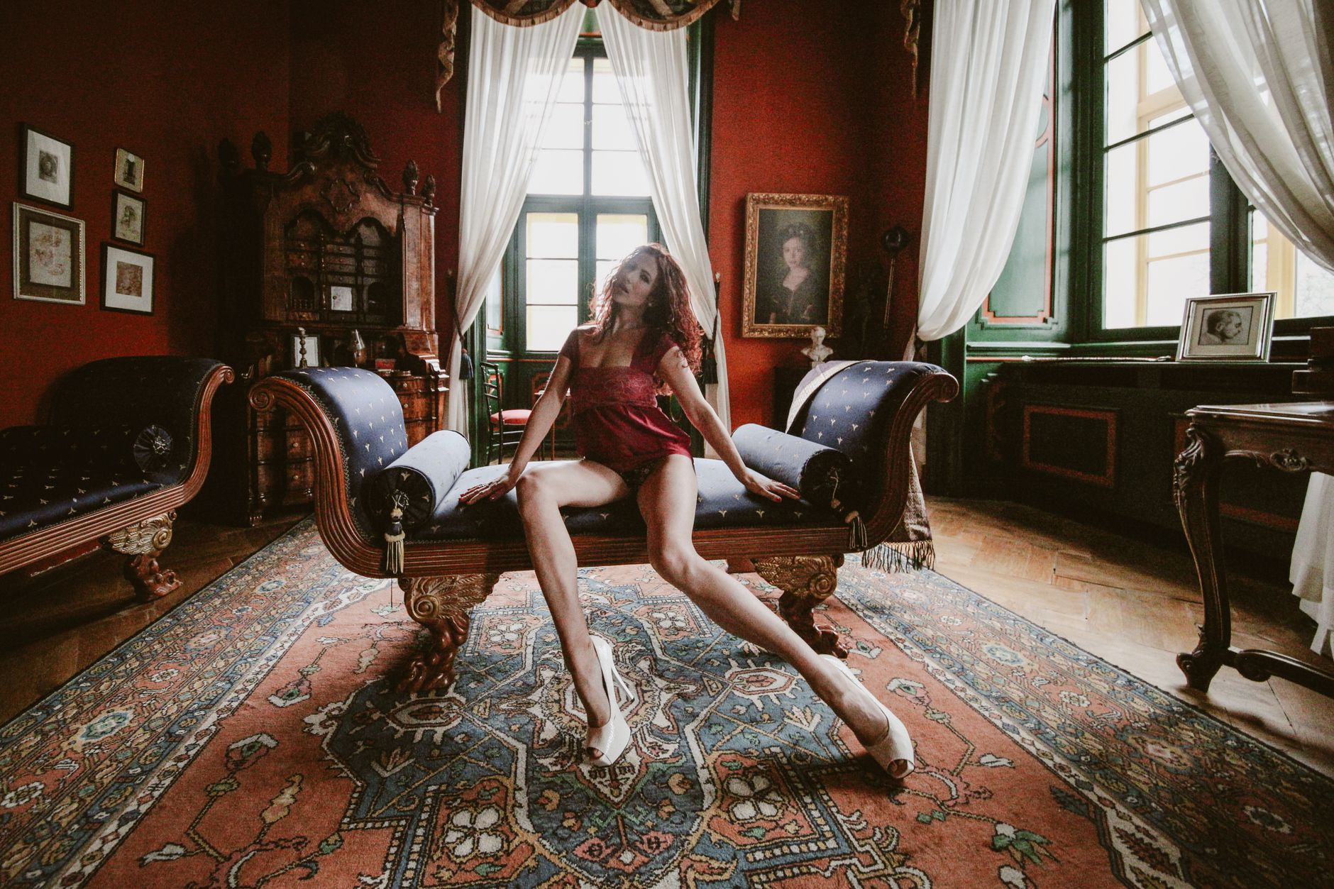 A woman in lingerie poses elegantly on an antique sofa in a vintage interior.