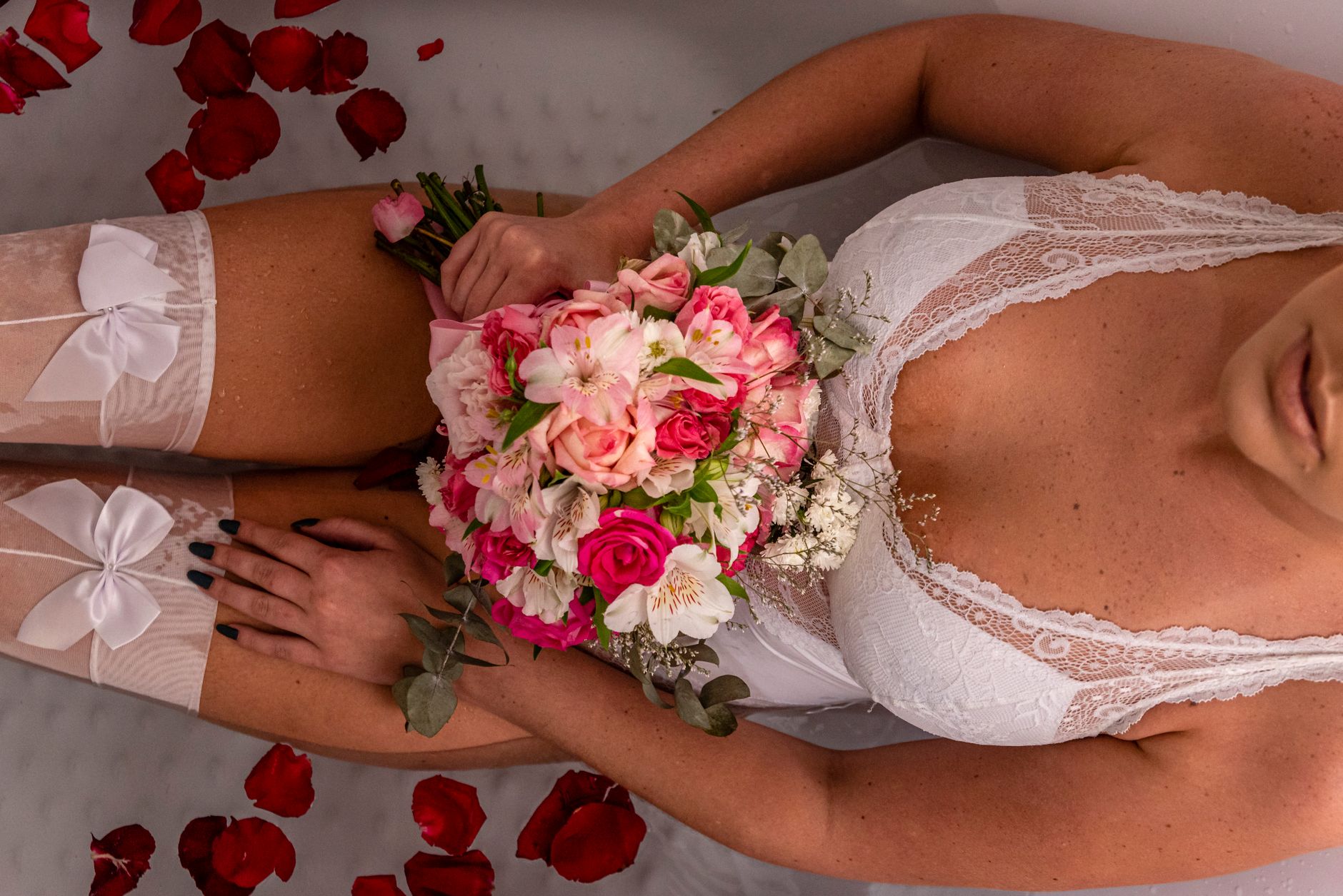Woman in white lingerie holding vibrant pink floral bouquet, surrounded by rose petals.