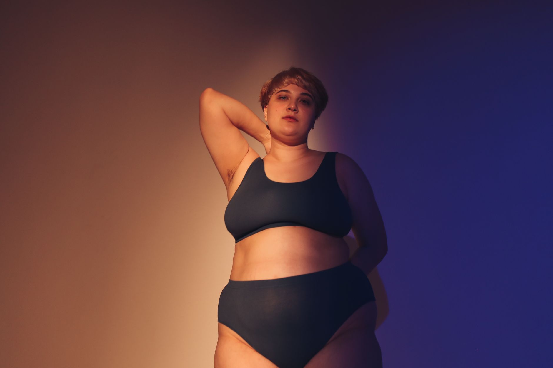 Confident plus size woman embraces body positivity in a studio setting with artistic lighting.