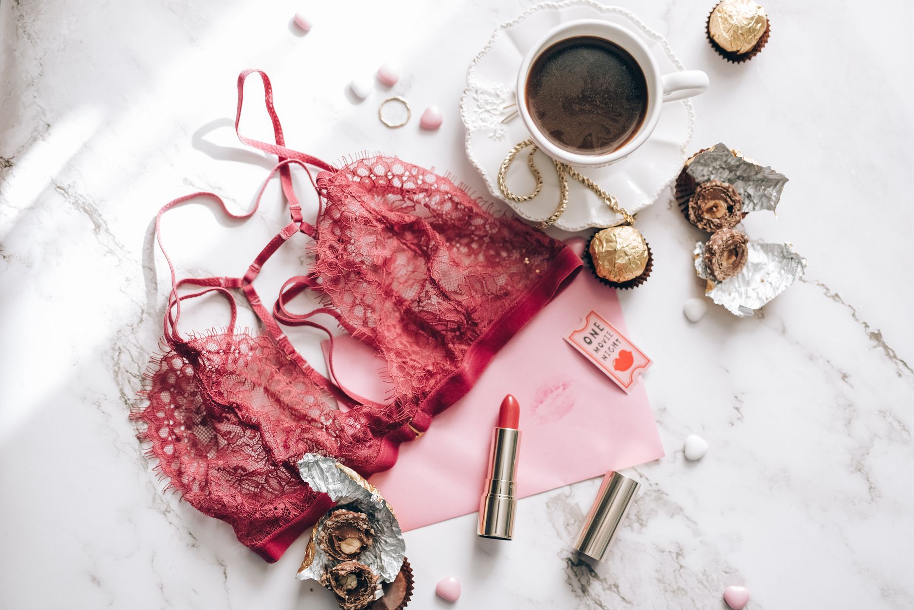A chic flat lay featuring coffee, chocolates, and lace lingerie on a marble surface.