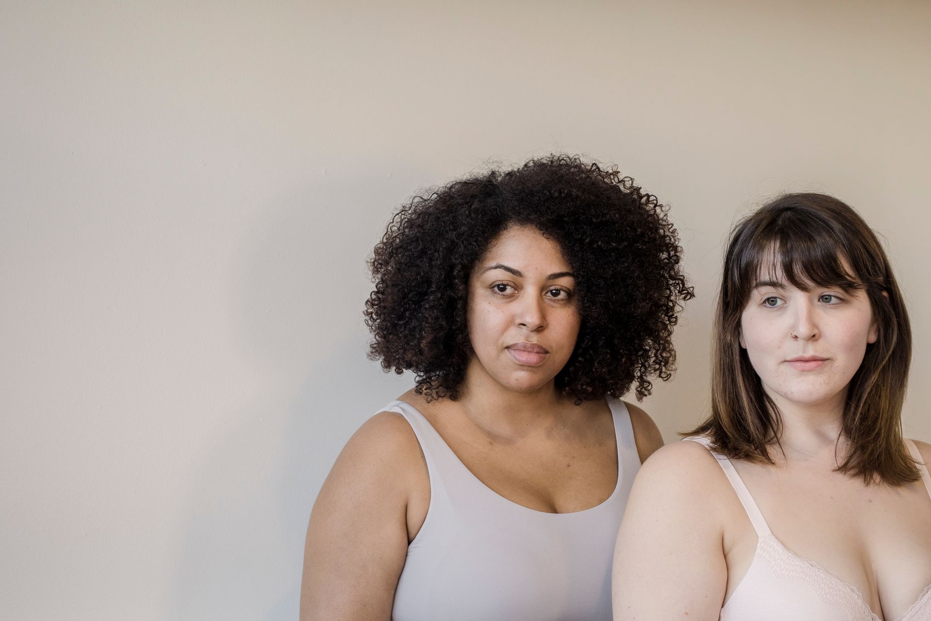 Adult overweight African American woman with curly hair against model in brassiere looking away