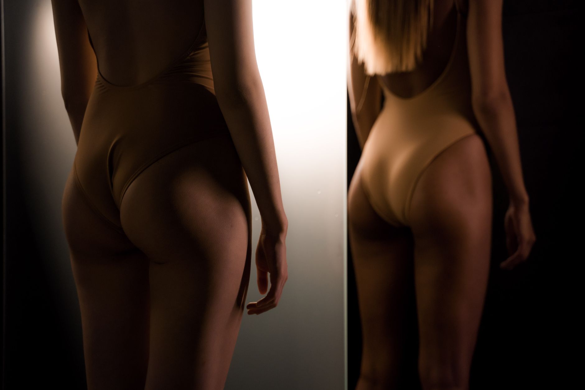 Elegant back view of a woman in a swimsuit with dramatic lighting and reflection.