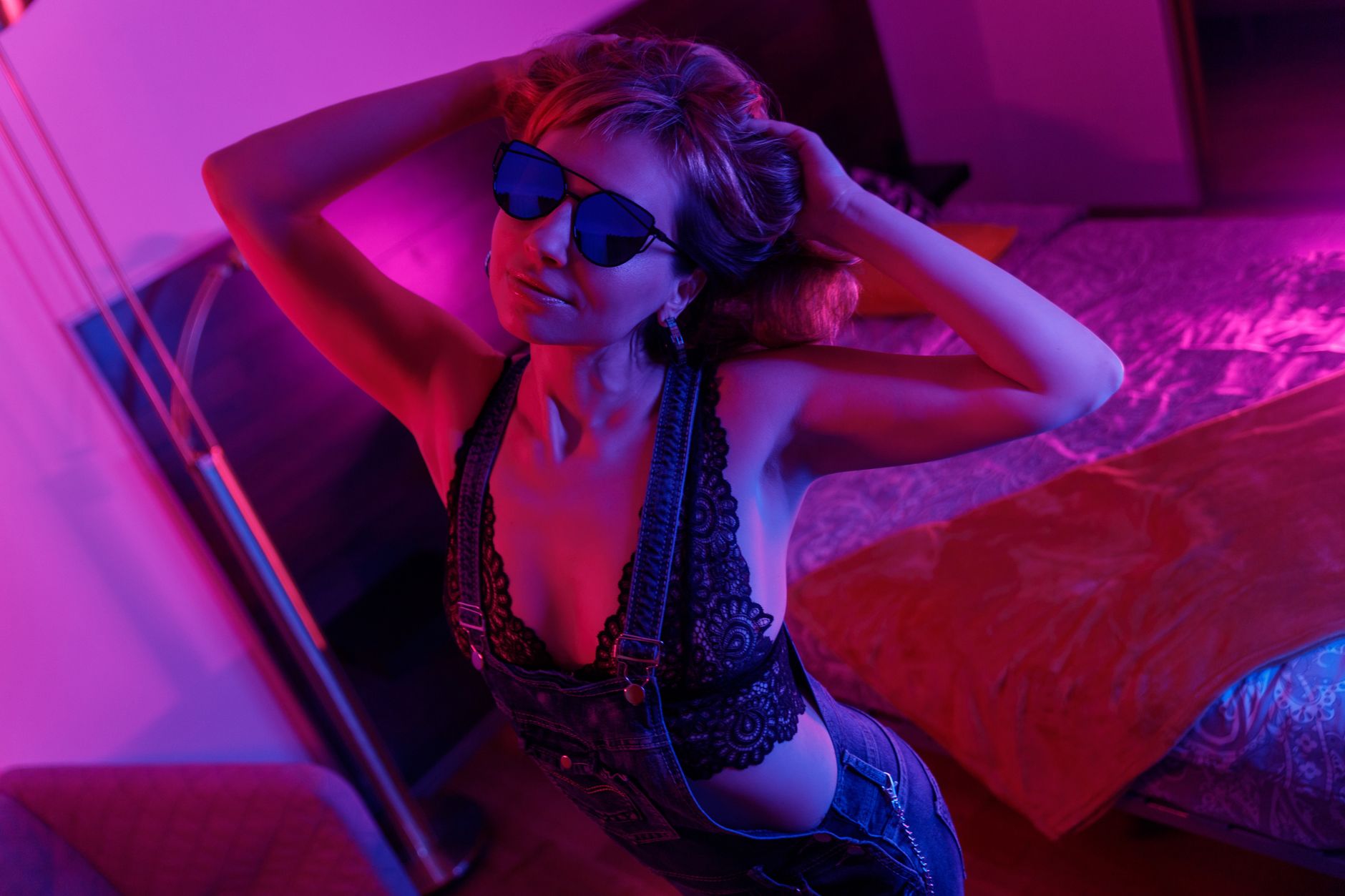 Woman wearing sunglasses in a fashionable pose, illuminated by vibrant neon lighting indoors.