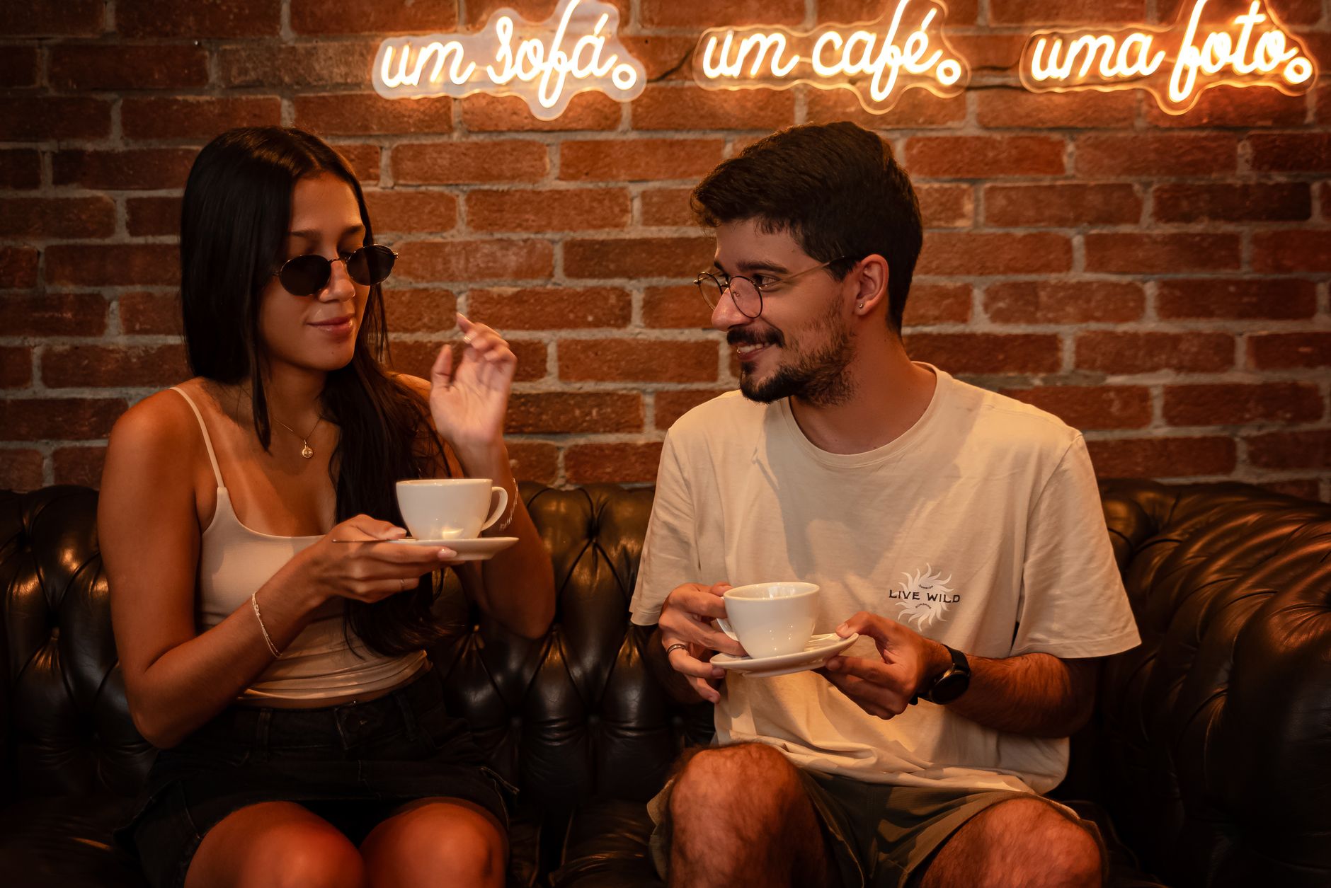 A couple enjoying coffee together in a relaxed, cozy café setting with neon signs.