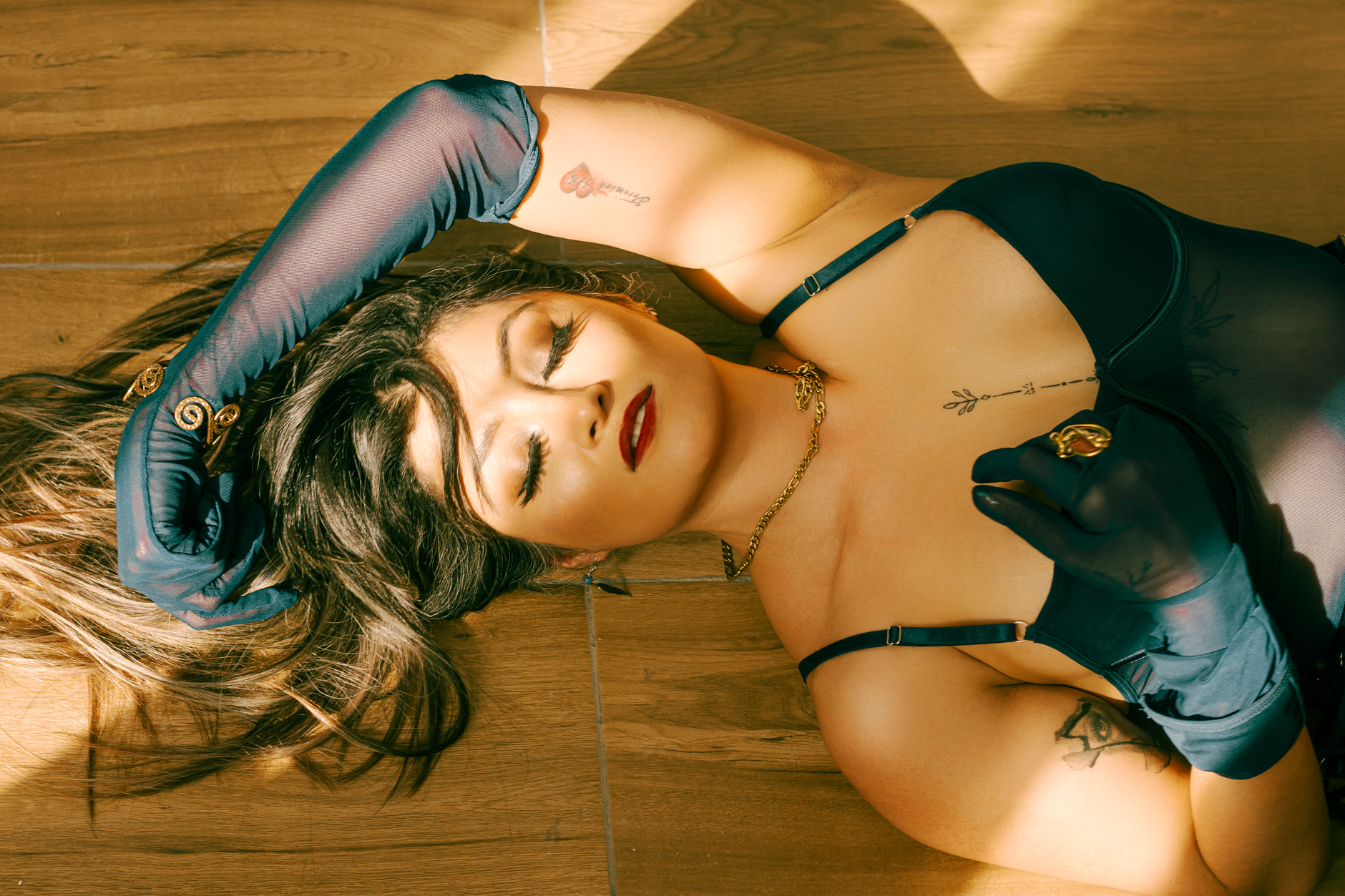 A woman elegantly posing on a wooden floor wearing dark lingerie and gloves, evoking fashion and sophistication.