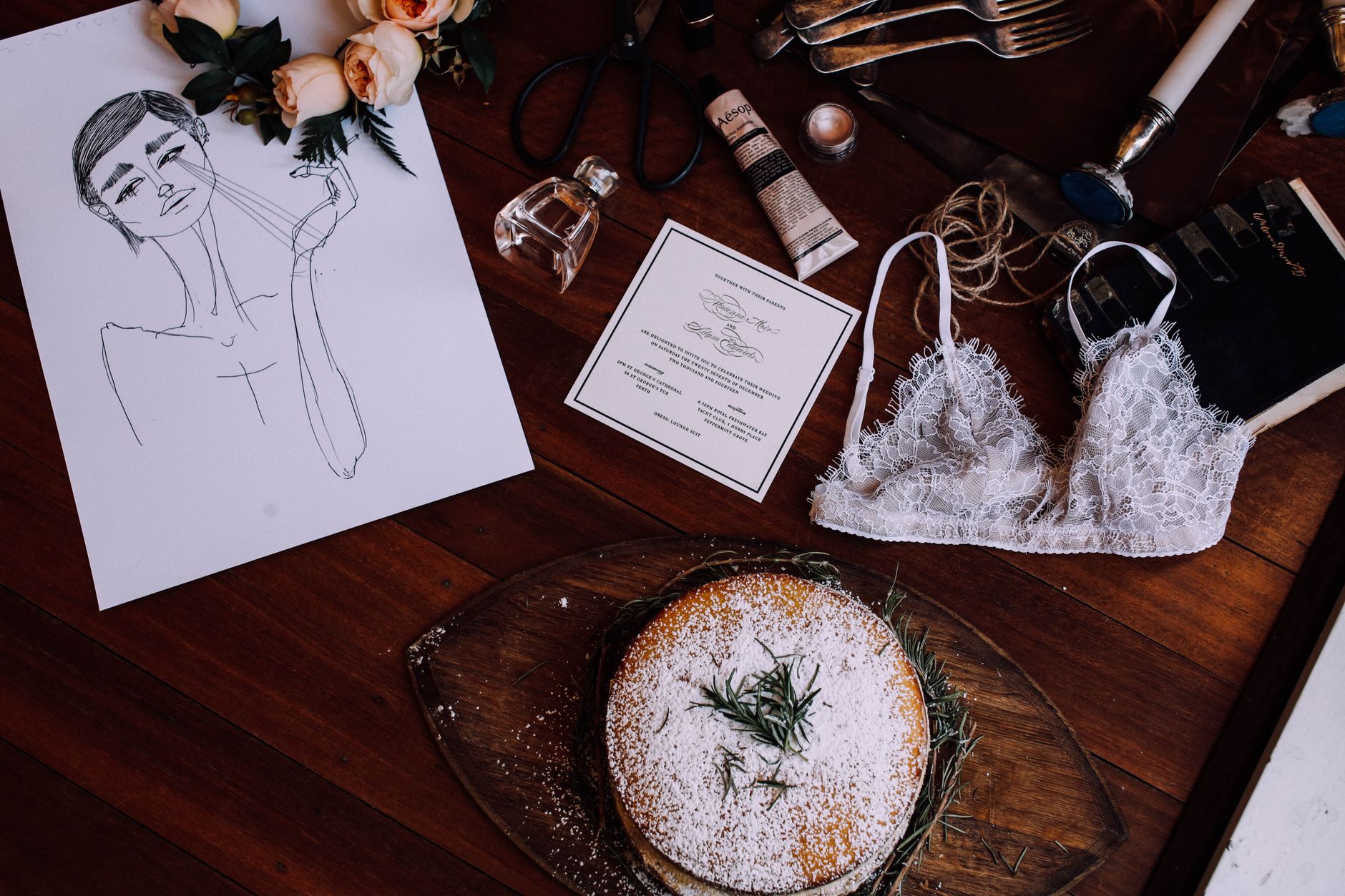 Top view composition of sweet fresh cake placed on wooden vanity table near lace bra scattered cosmetics and sheet with drawing
