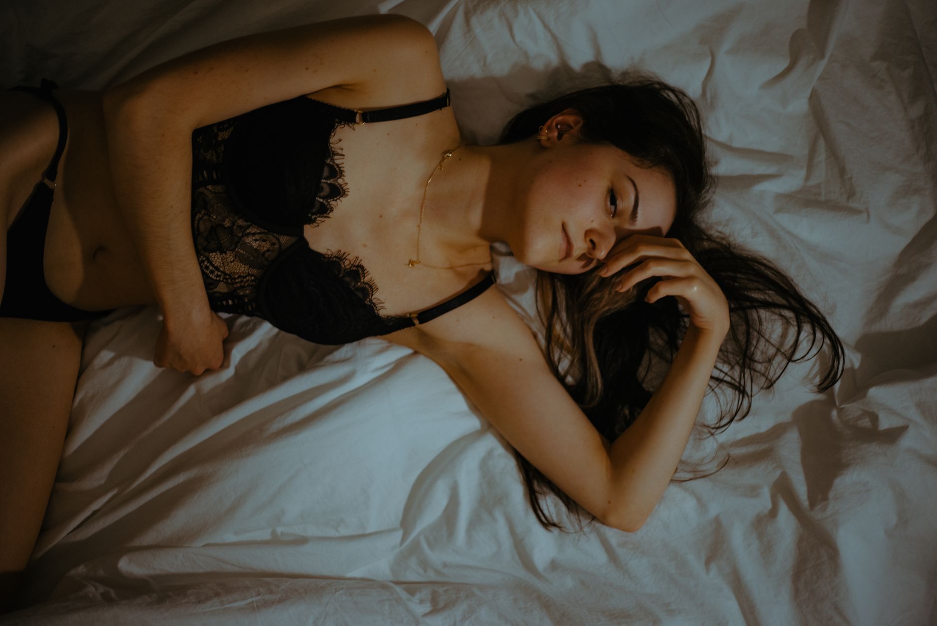 A woman in lingerie lying on a bed, captured in a serene and relaxed pose indoors.