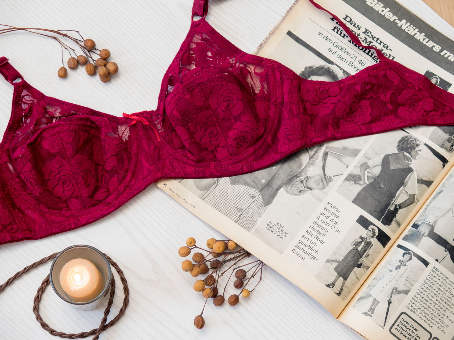 Elegant red lace brassiere displayed on a vintage magazine flat lay with candle and dried berries.