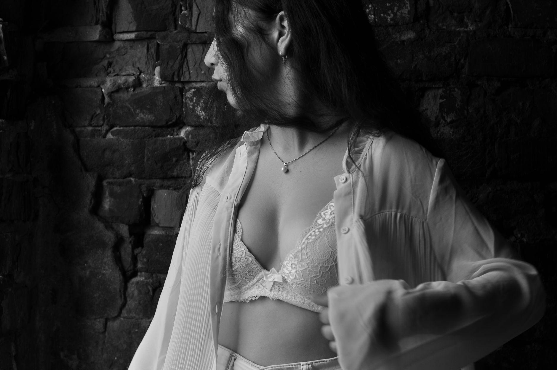 Moody black and white portrait of a woman in white apparel against a textured wall.