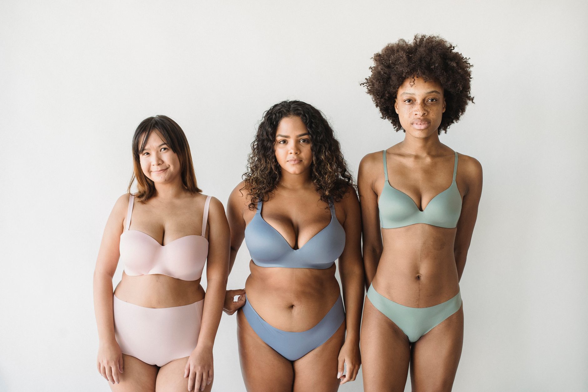 Three diverse women wearing stylish bras and panties posing confidently against a neutral background.