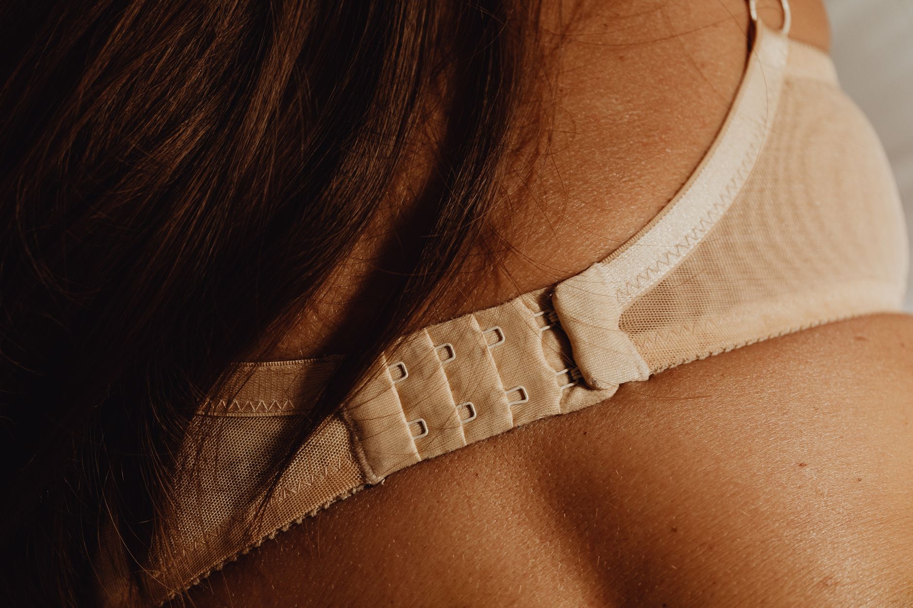 Intimate close-up of a beige bra clasp on skin, highlighting details and texture.