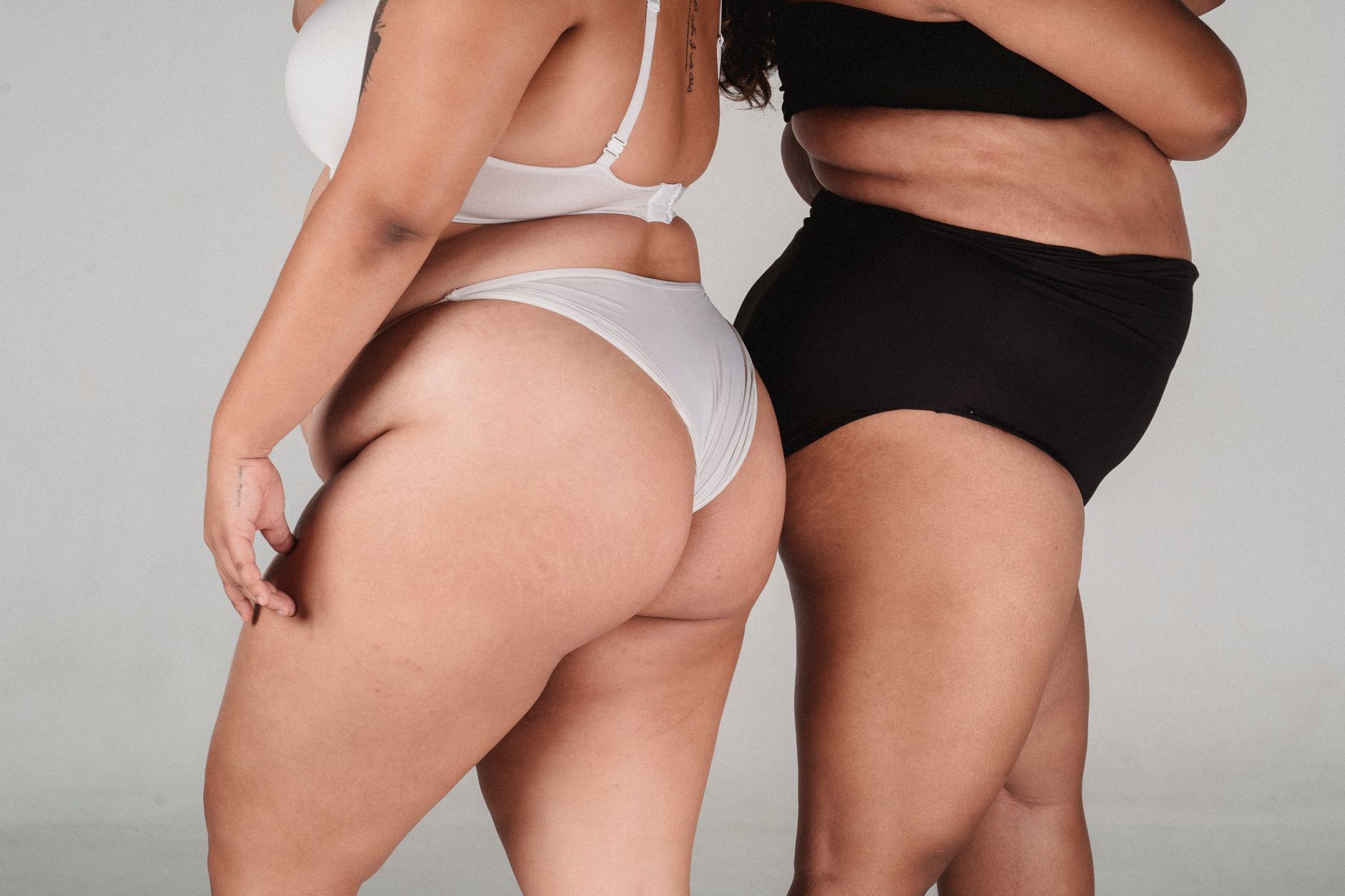 Side view of anonymous plus size female in black and white underwear standing back to back on white background in studio