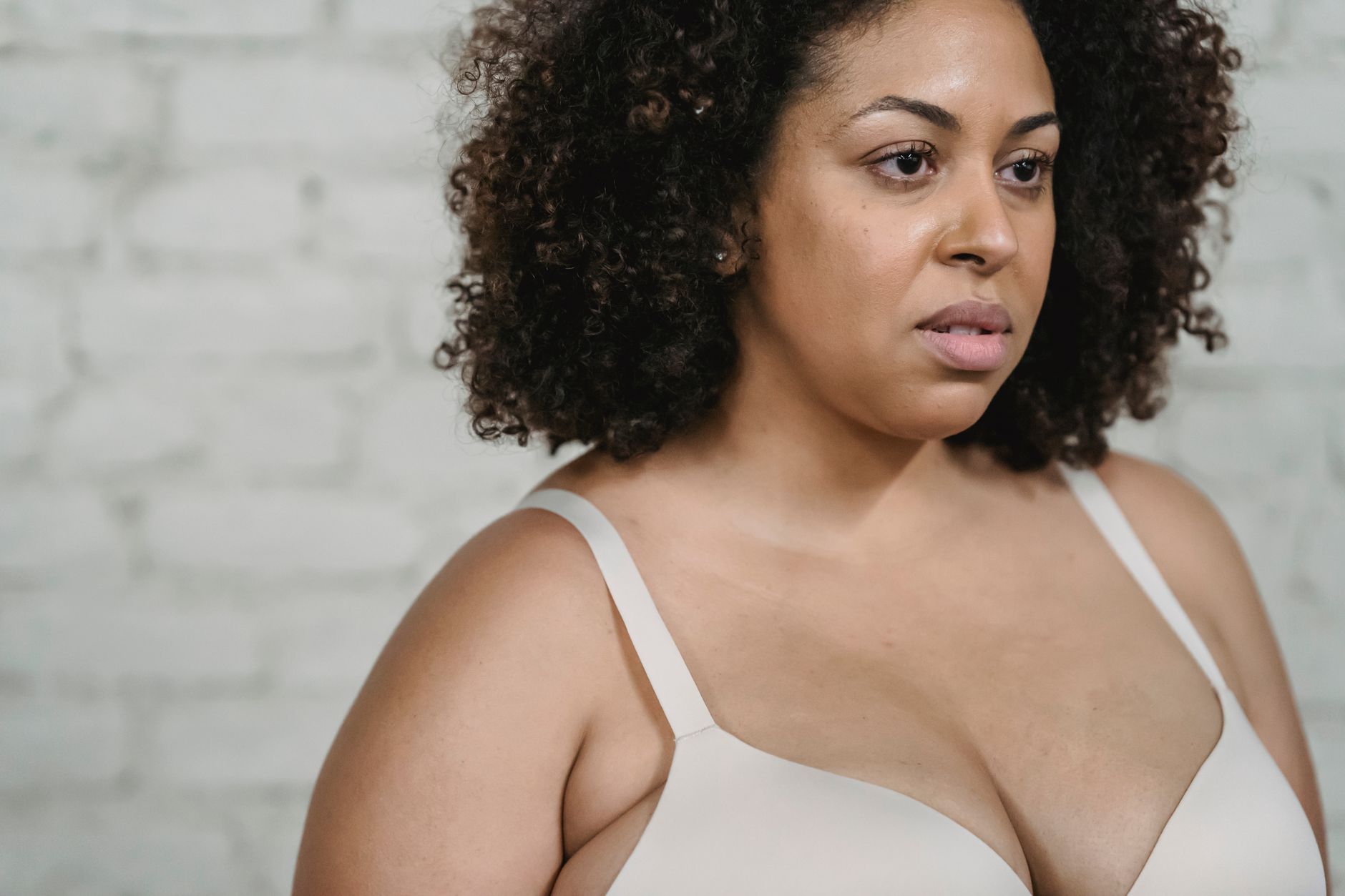 Serious ethnic adult plump female in white underwear near white brick wall in light room