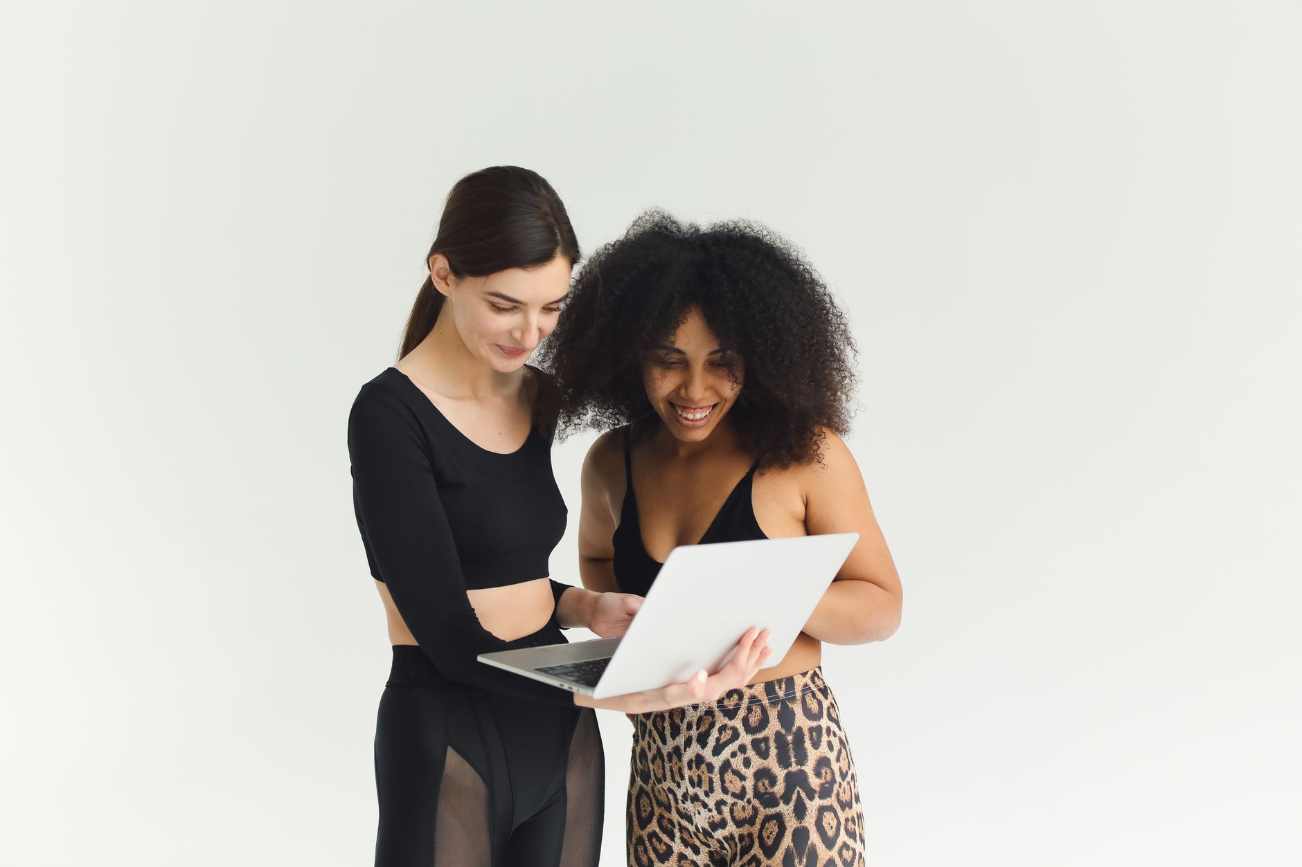 Two women in activewear sharing ideas while using a laptop, showcasing teamwork and diversity.