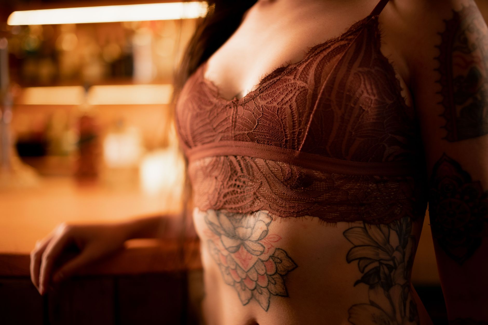 Intimate close-up of a woman's torso with tattoos, showcasing intricate lace lingerie.