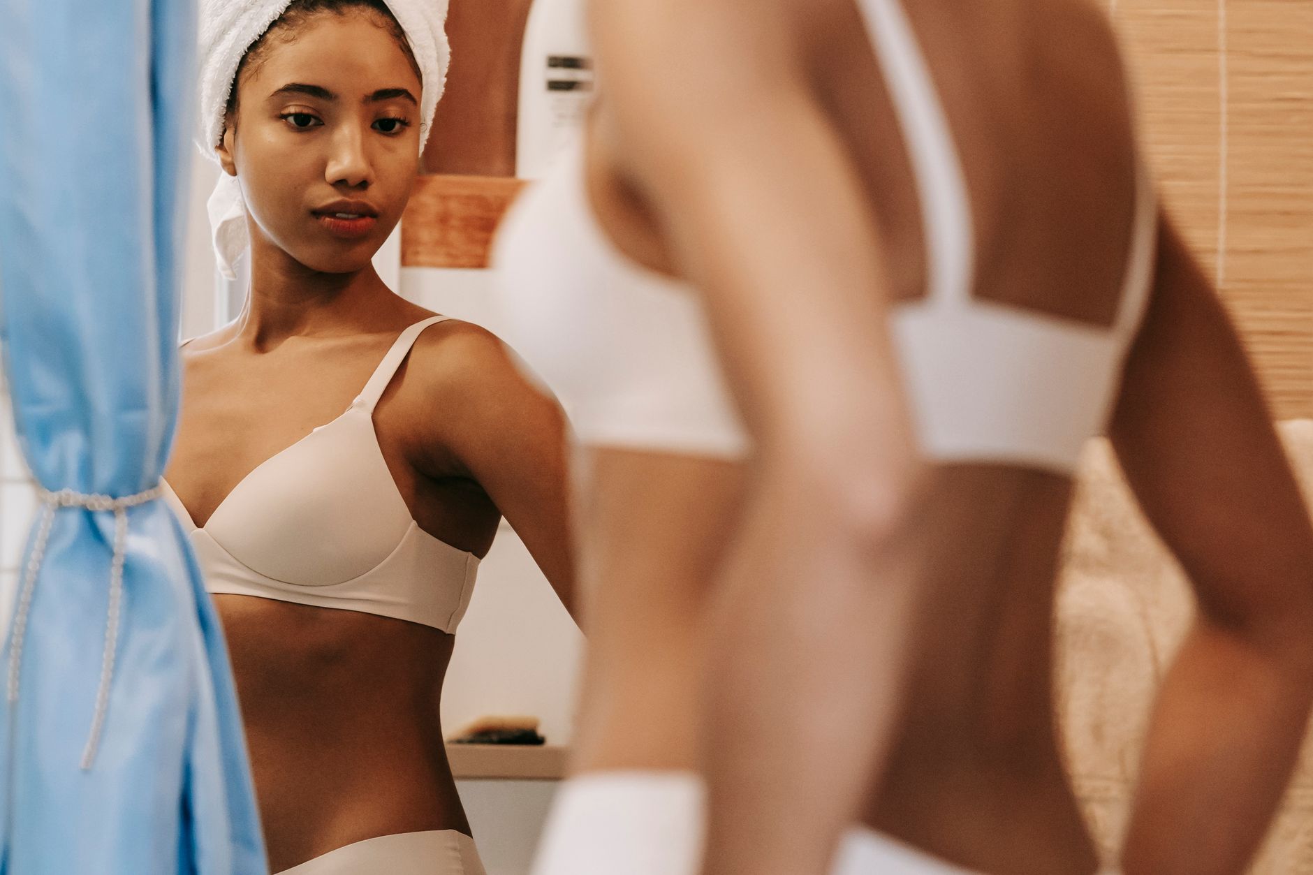Serious ethnic female in turban standing in underwear and looking at curves of figure in bathroom