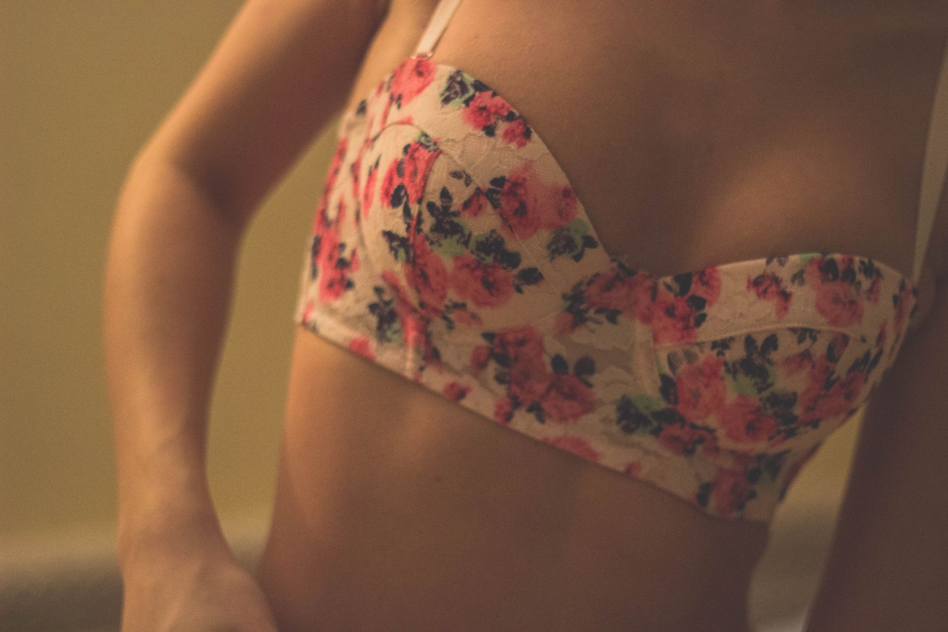 Intimate close-up of a woman wearing a floral patterned bra indoors. Soft lighting enhances the mood.