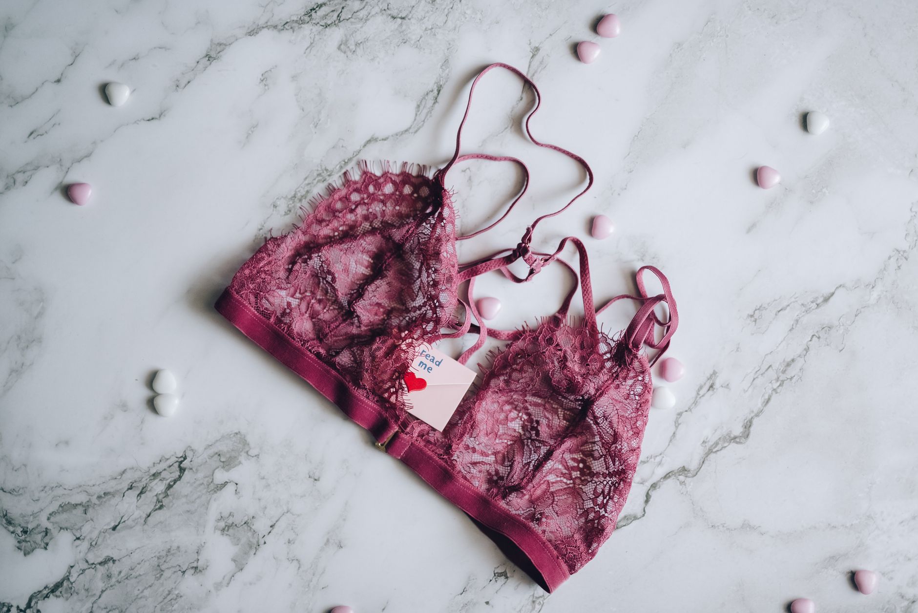A stylish lace bra on a marble background surrounded by small hearts, captured in a flat lay style.