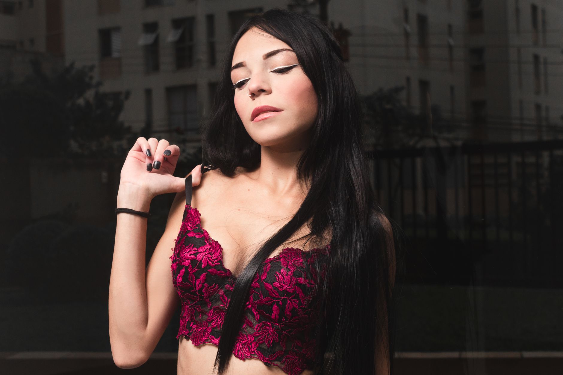 Stylish woman with dark hair wearing a pink lace brassiere poses confidently outdoors.