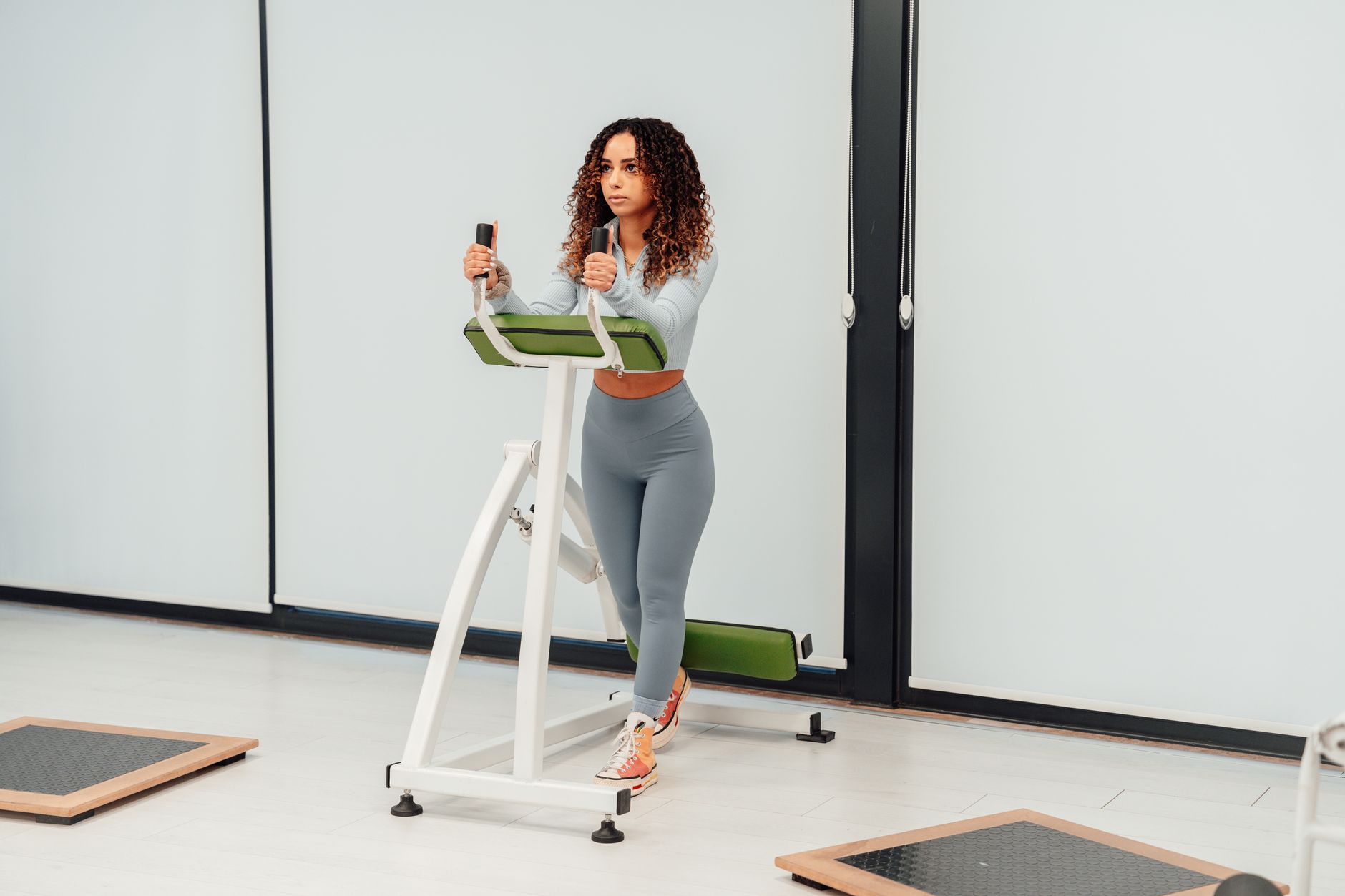 A woman with curly hair exercises on a machine in a bright gym.