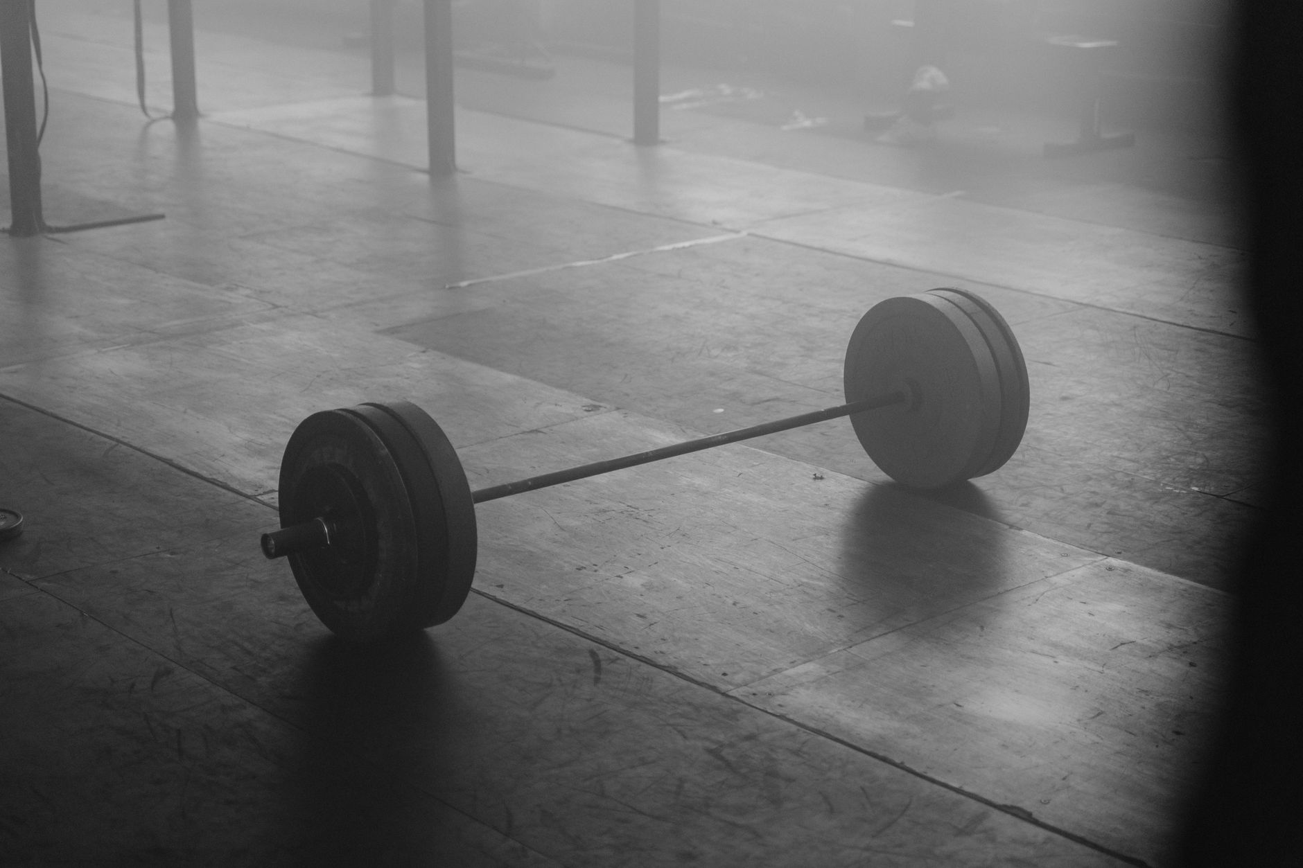 Monochrome image of a barbell resting on a gym floor, exuding stillness.